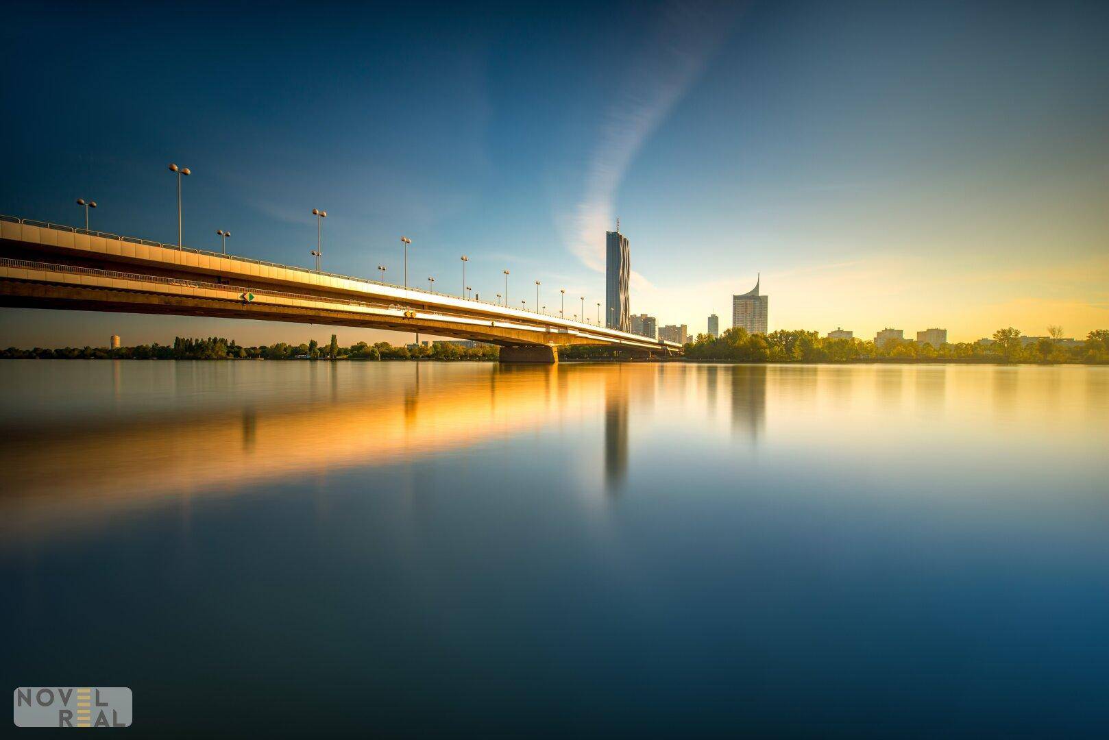 Morgenstimmung am Fluss mit Brücke und der Silhouette der Stadt im goldenen Licht.