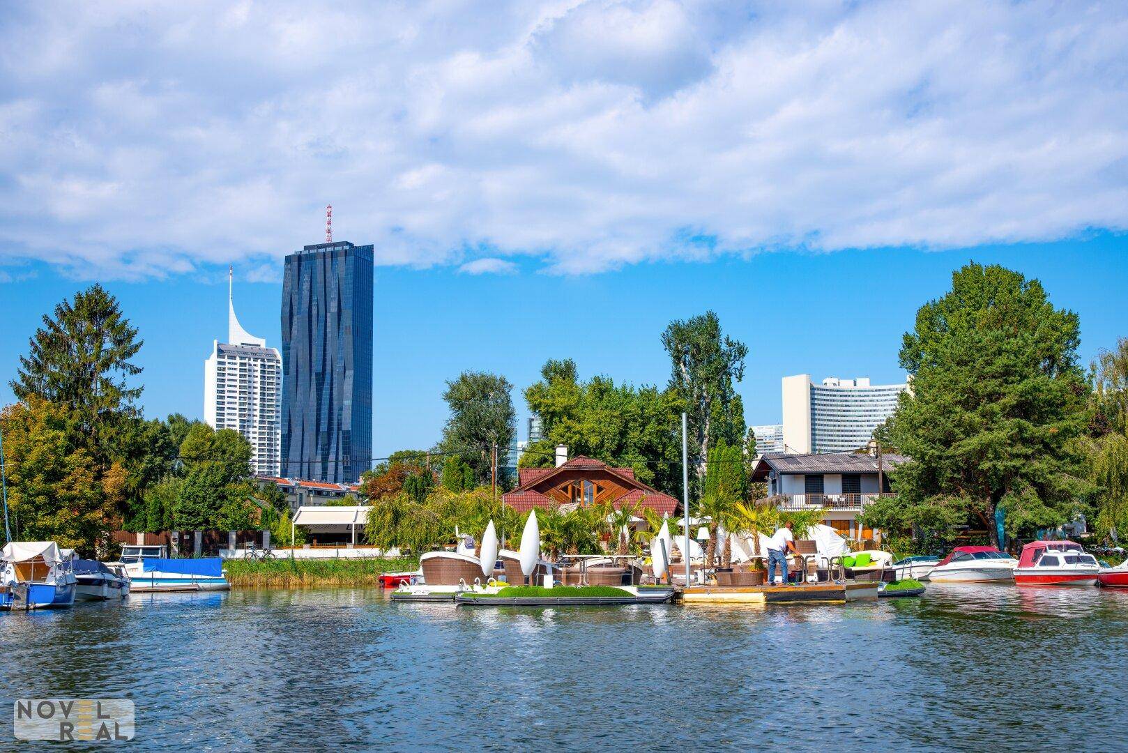 Blick auf den See mit Booten und der städtischen Skyline im Hintergrund an einem sonnigen Tag.