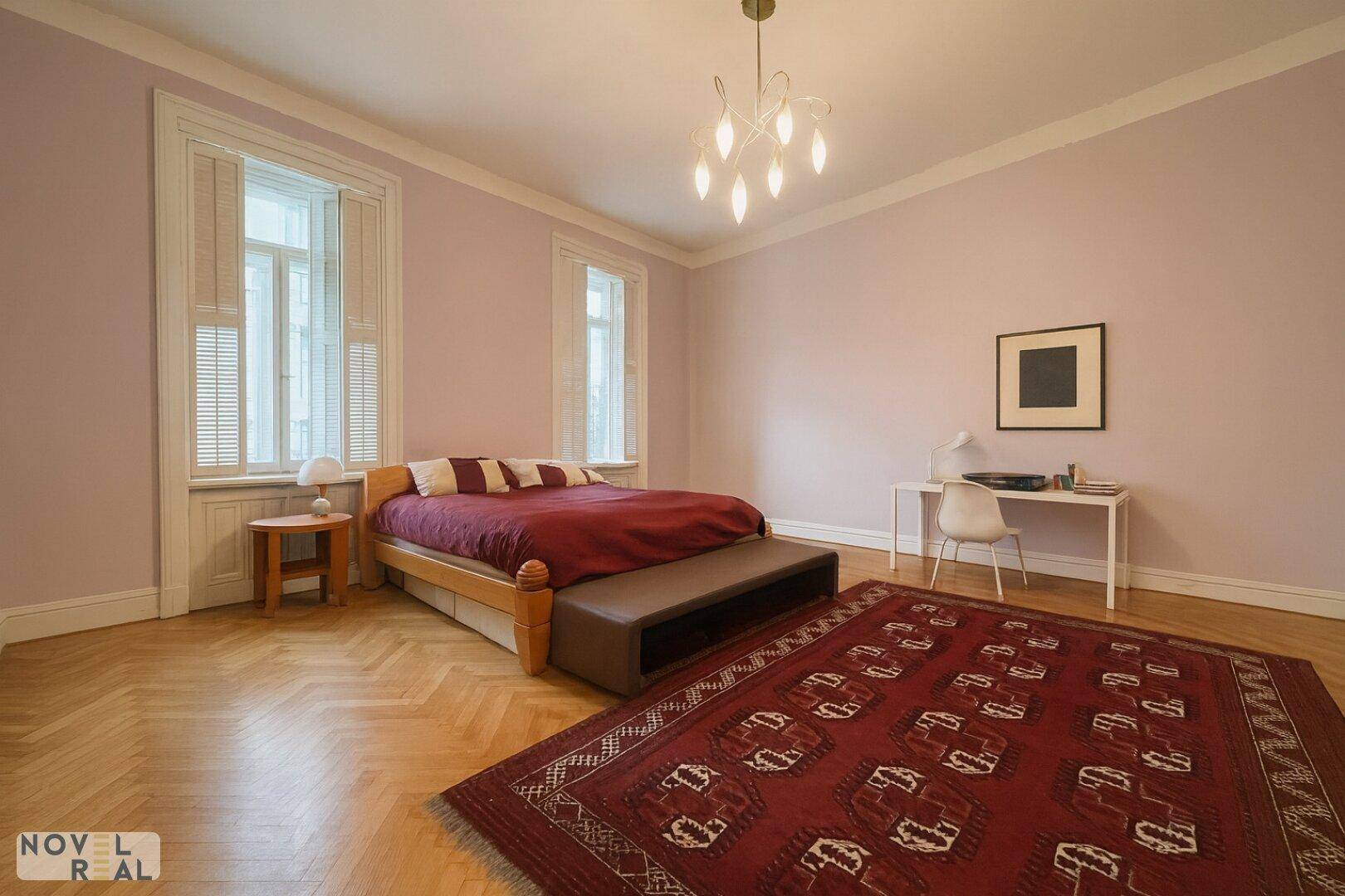 Geräumiges Schlafzimmer mit Holzbett, Schreibtisch und traditionellem Teppich auf Parkettboden.