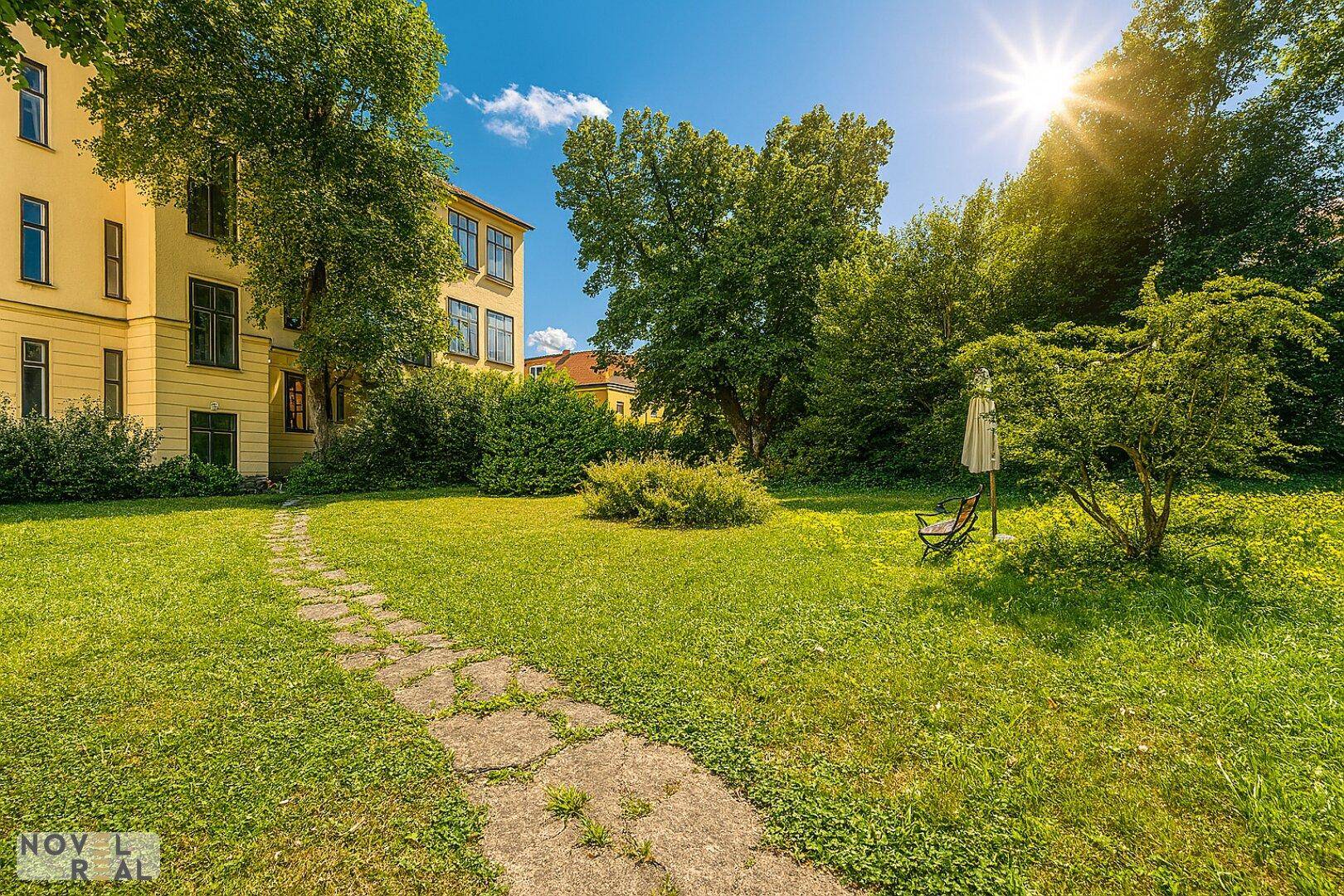 Gepflegter Gartenbereich mit Rasenfläche und Steinweg vor dem historischen Gebäude.