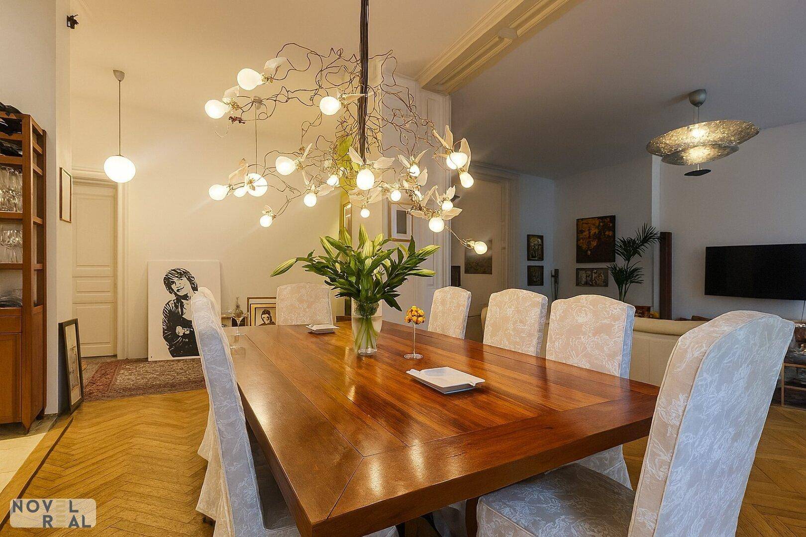 Eleganter Essbereich mit großem Holztisch, Designer-Kronleuchter und Blick in den angrenzenden Wohnbereich.