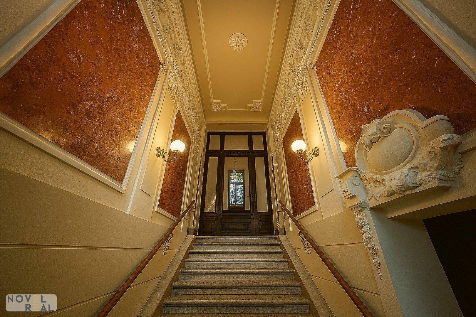 Elegantes Treppenhaus mit Stuckverzierungen, Marmorwänden und klassischer Beleuchtung in einem historischen Gebäude.