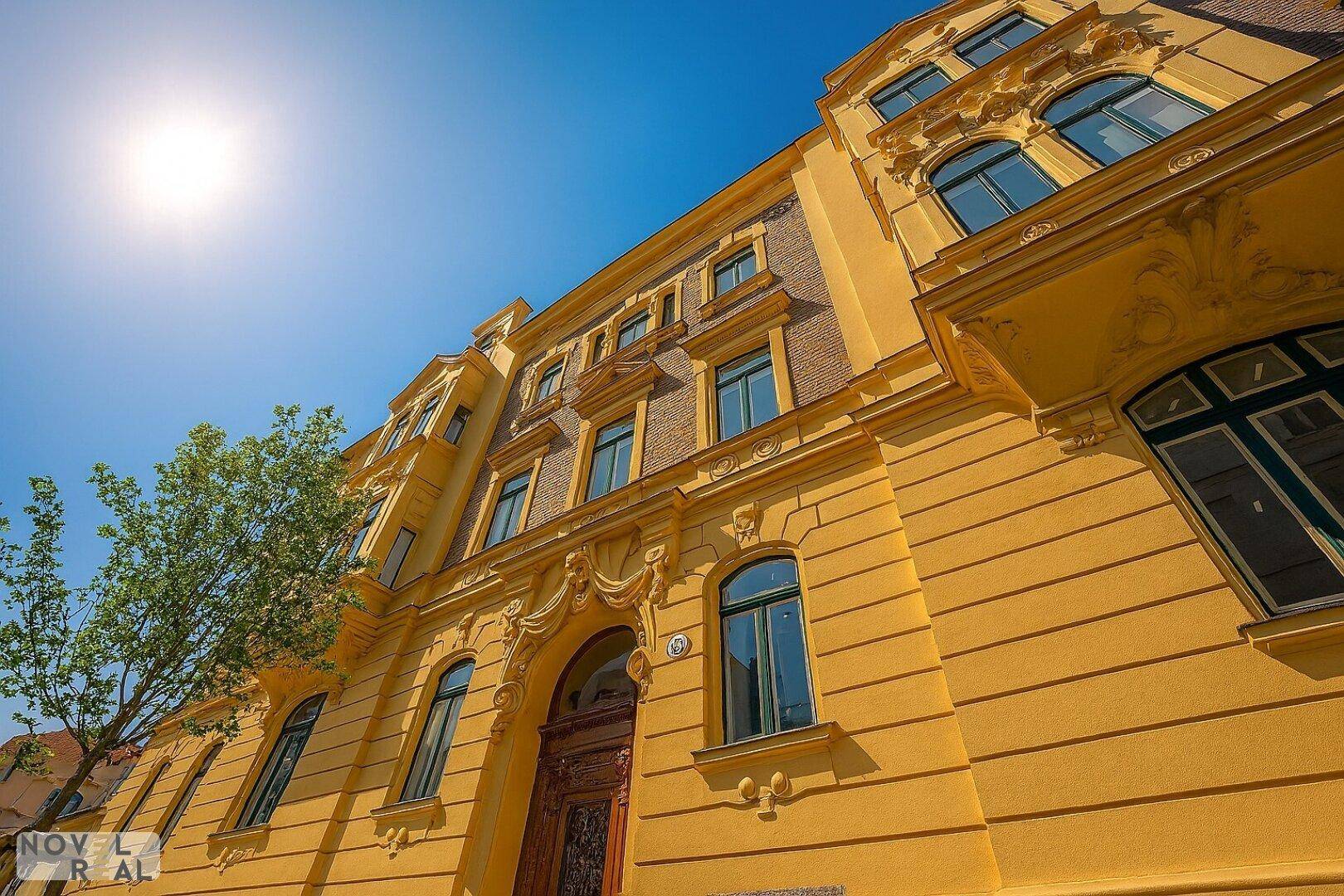 Prächtige historische Fassade mit aufwendigen Verzierungen und gelbem Anstrich unter blauem Himmel.