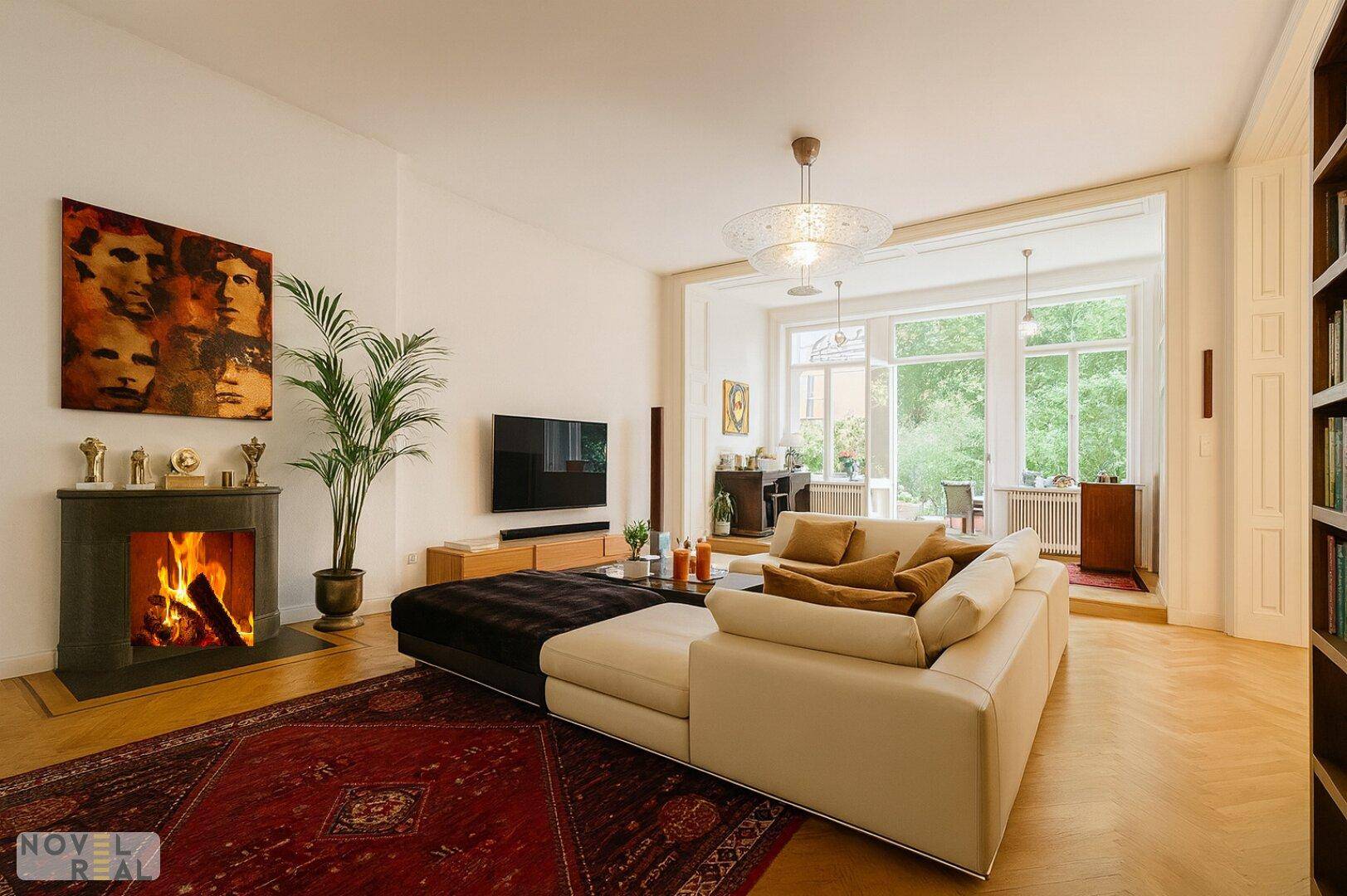 Helles Wohnzimmer mit Kamin, bequemer Sitzecke und Blick auf den angrenzenden Bereich mit großen Fenstern.