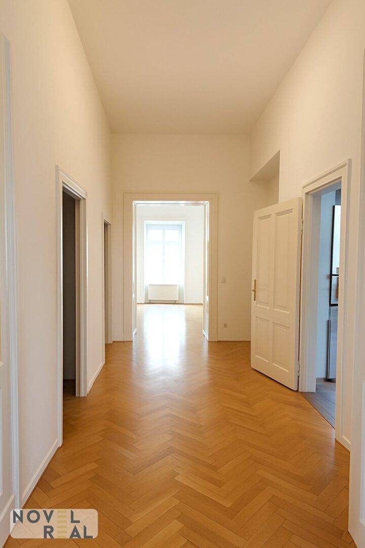 Langer, heller Flur mit Fischgrätparkett, der zu verschiedenen Räumen führt.