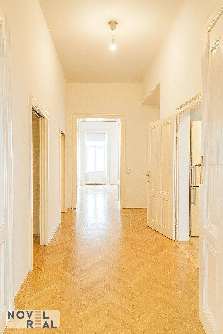 Heller Flur mit Fischgrätparkett und Deckenleuchte, der zu den Wohnbereichen führt.