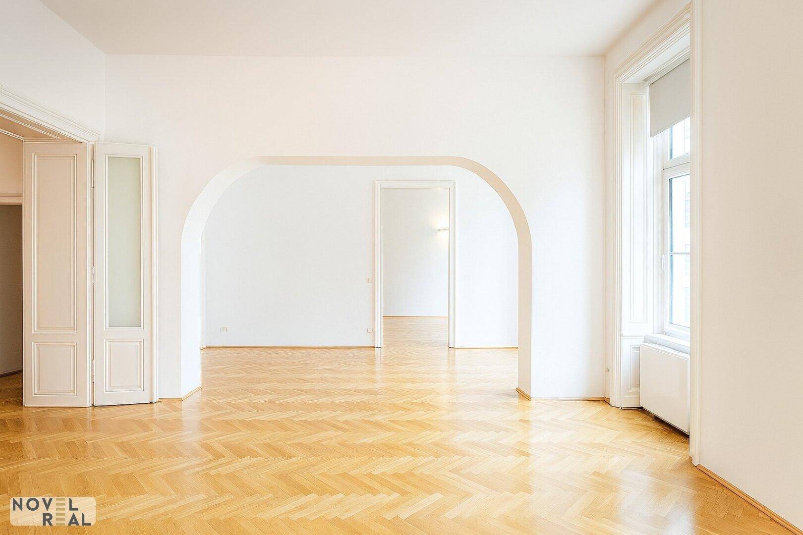 Geräumiger Wohnbereich mit Fischgrätparkett und eleganten Rundbögen, der mehrere Zimmer verbindet.