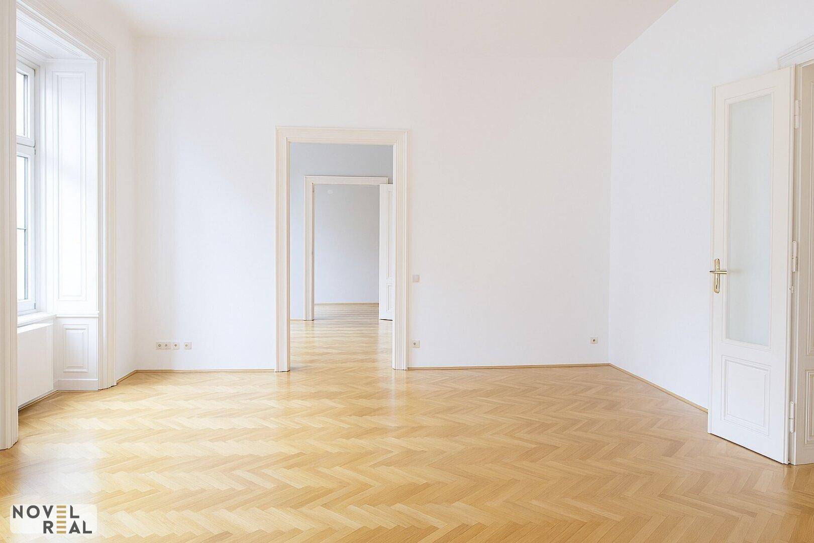 Heller Raum mit Fischgrätparkett und hohen Decken, der einen weiten Blick in den Flur bietet.
