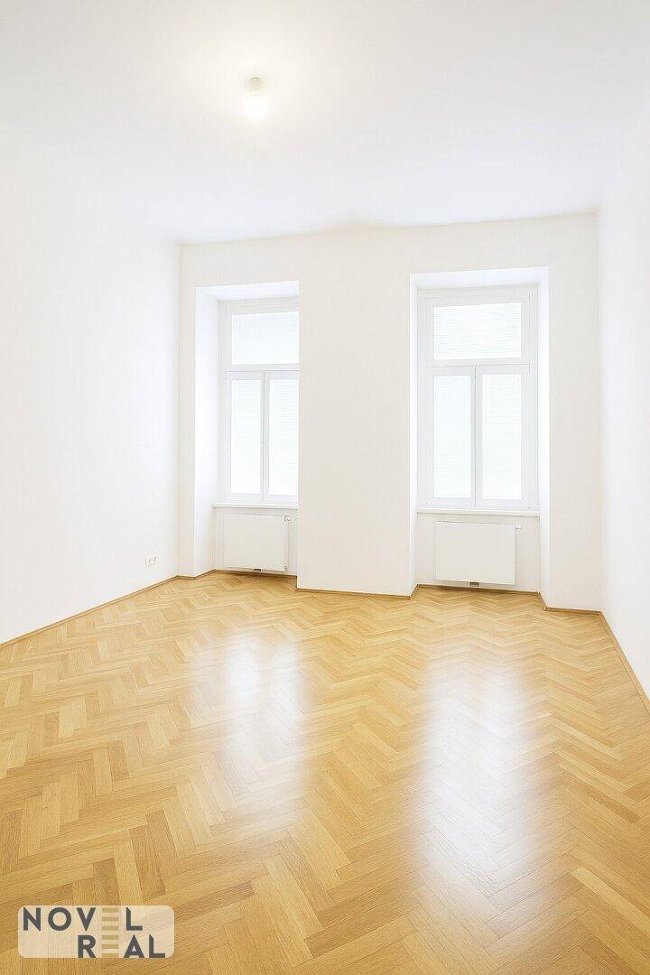Helles, leeres Zimmer mit Fischgrätparkett und großen Fenstern, bereit zur Einrichtung.