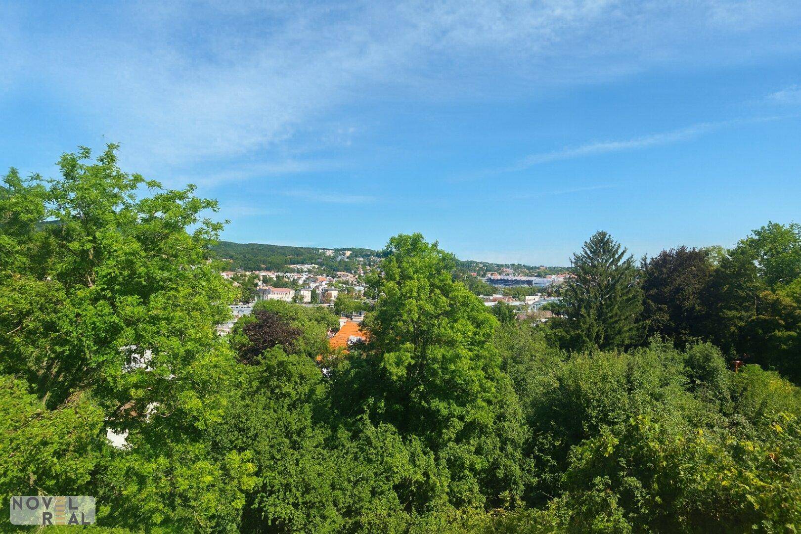 Panoramablick über eine Stadtlandschaft, umgeben von üppigem Grün unter klarem Himmel.