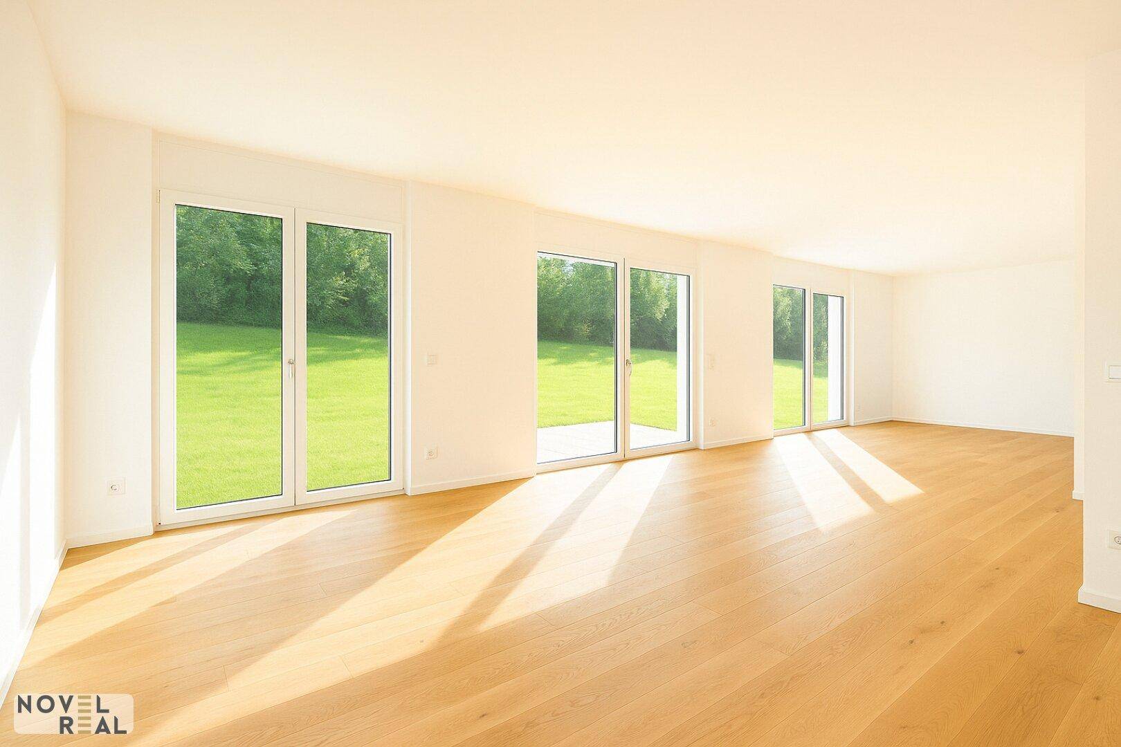 Lichtdurchfluteter Wohnbereich mit Holzboden und mehreren Fenstern mit Blick ins Grüne.