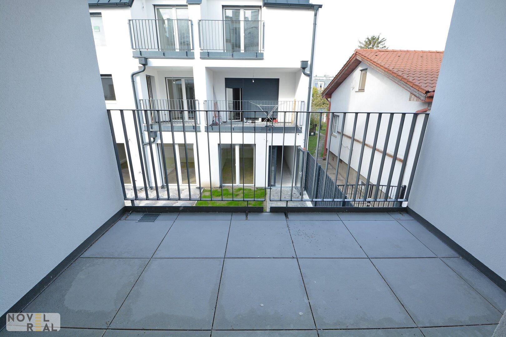 Moderner Balkon mit Fliesenboden und Blick auf den begrünten Innenhof und die Nachbarschaft.