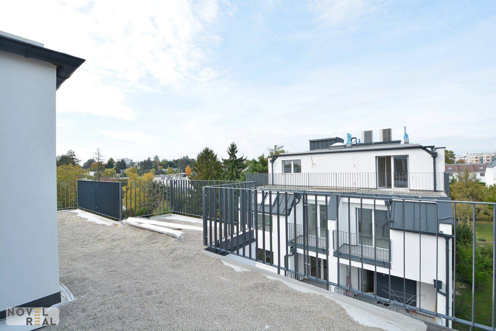 Im Bau befindliche Dachterrasse eines Neubaus mit Blick auf die umliegende Bebauung und Natur.