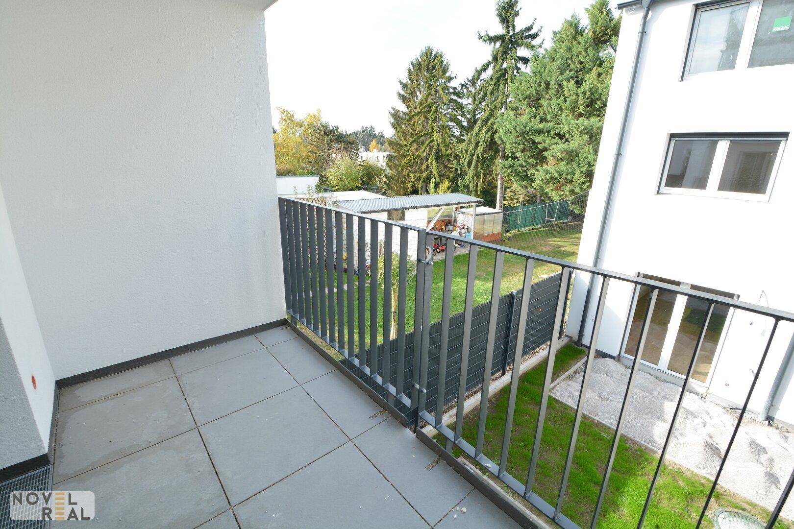Geräumiger Balkon mit Fliesenboden und Metallgeländer, bietet Blick auf den grünen Gartenbereich.