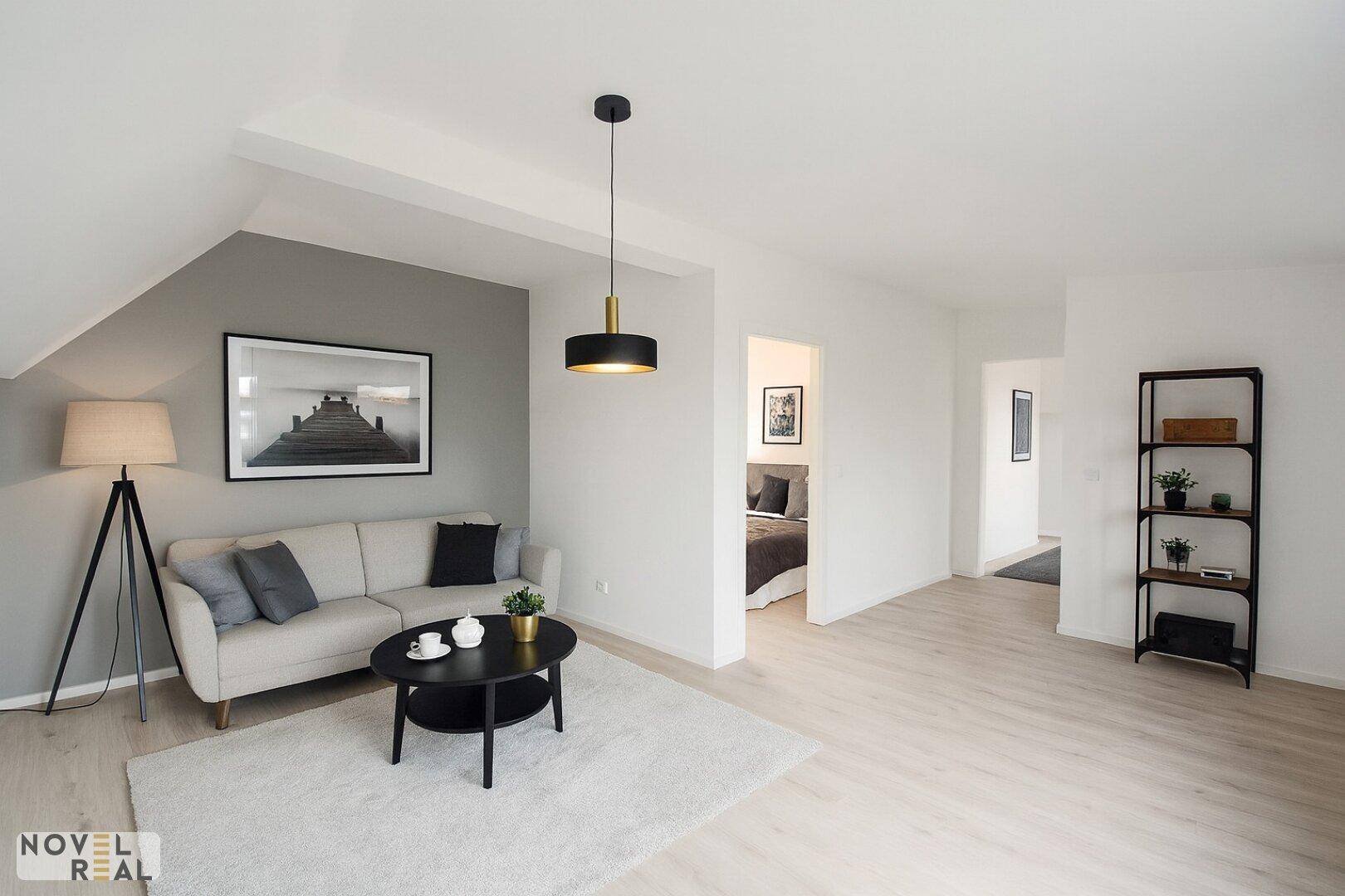 Helles und modern eingerichtetes Wohnzimmer mit hellem Holzboden und Blick in ein Schlafzimmer.