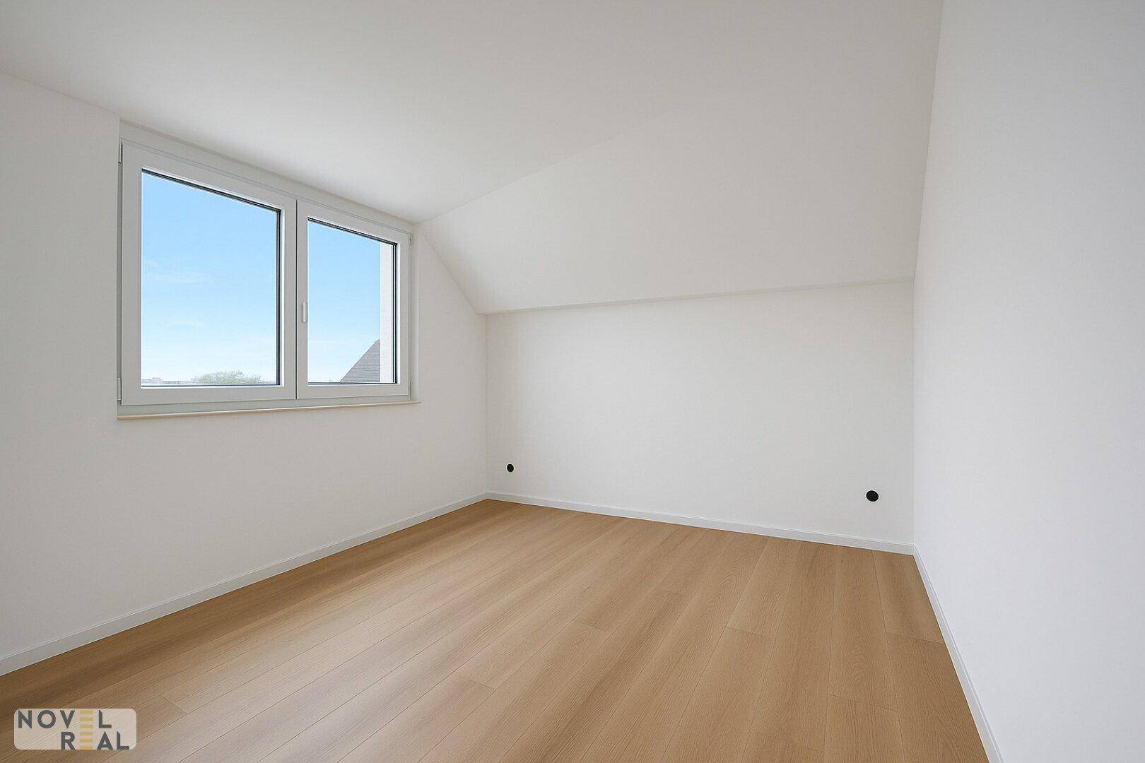 Helles Schlafzimmer mit Dachschräge, großem Fenster und neuem Holzfußboden.