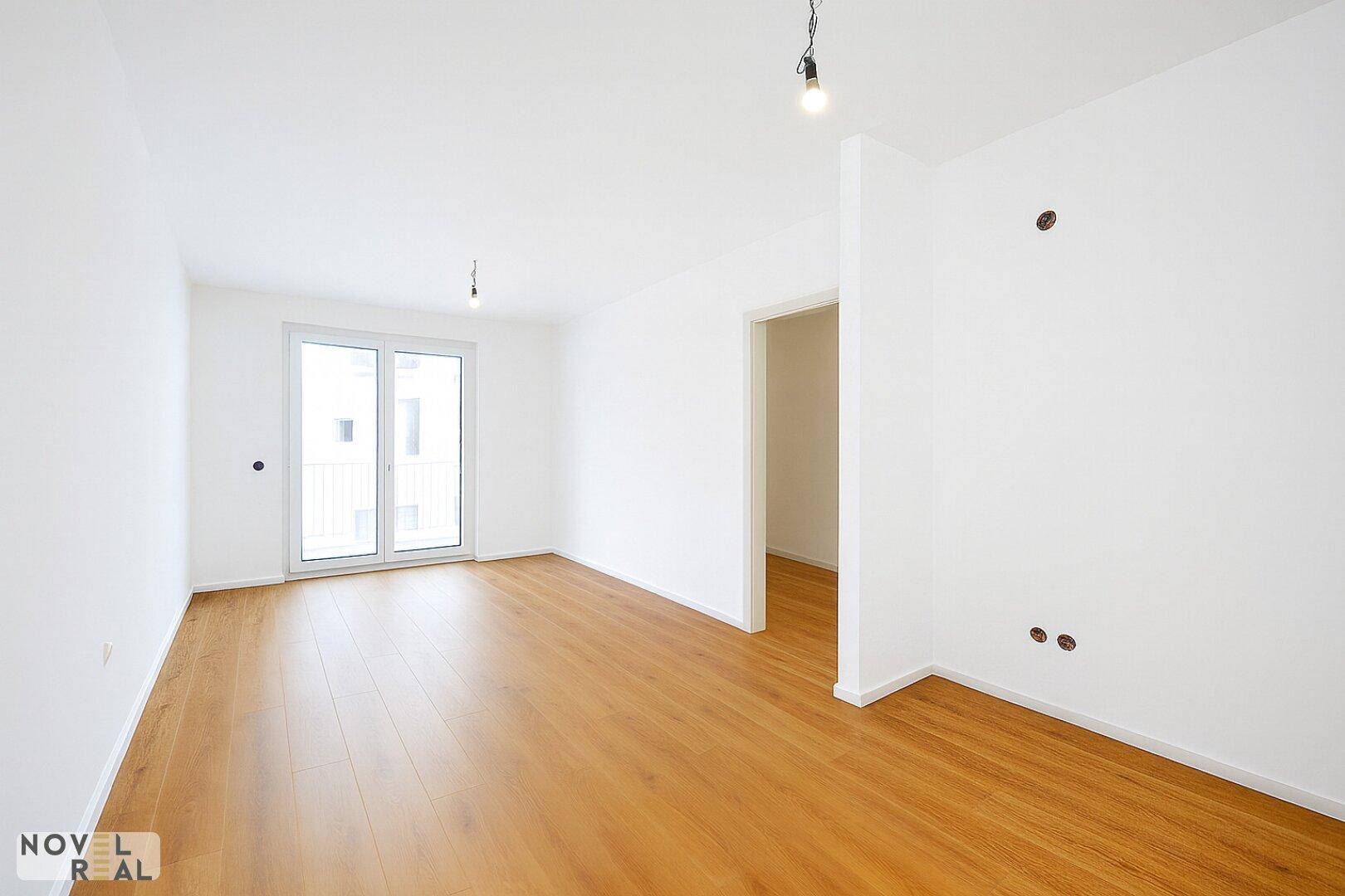 Geräumiger, leerer Raum mit hellem Holzboden und Zugang zu einem französischen Balkon, ideal zur individuellen Gestaltung.