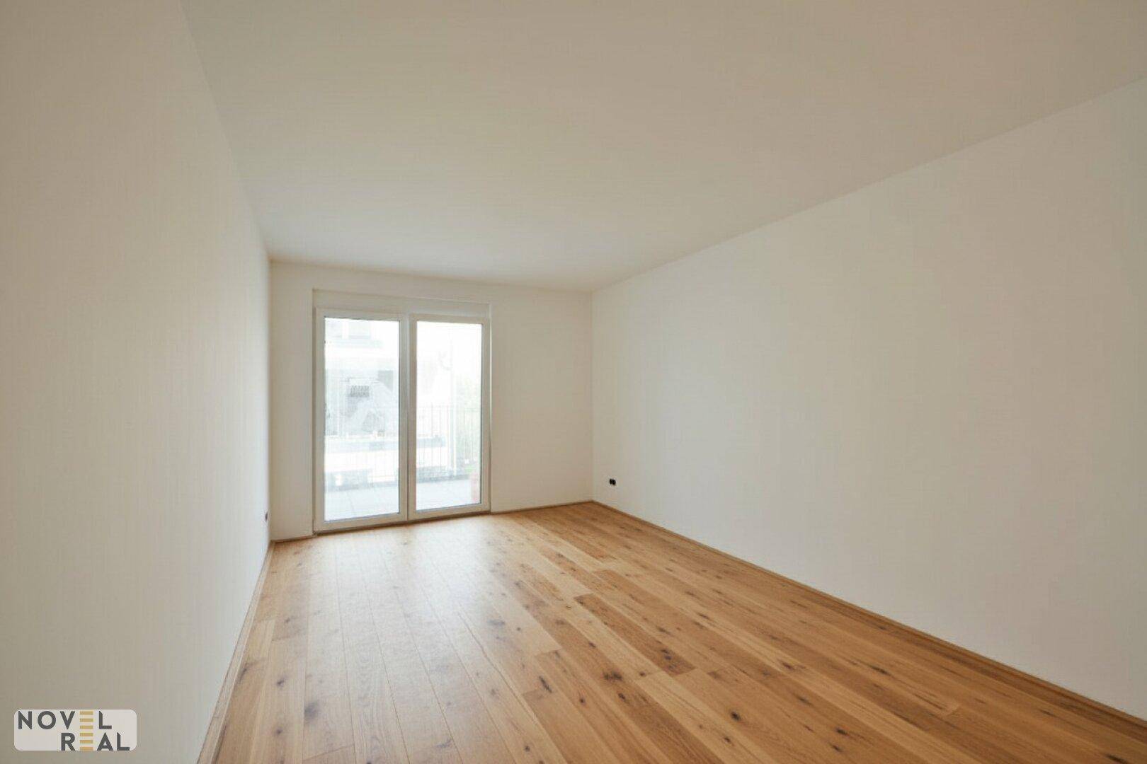 Lichtdurchfluteter Raum mit Holzfußboden und Zugang zu einem Balkon oder einer Terrasse.