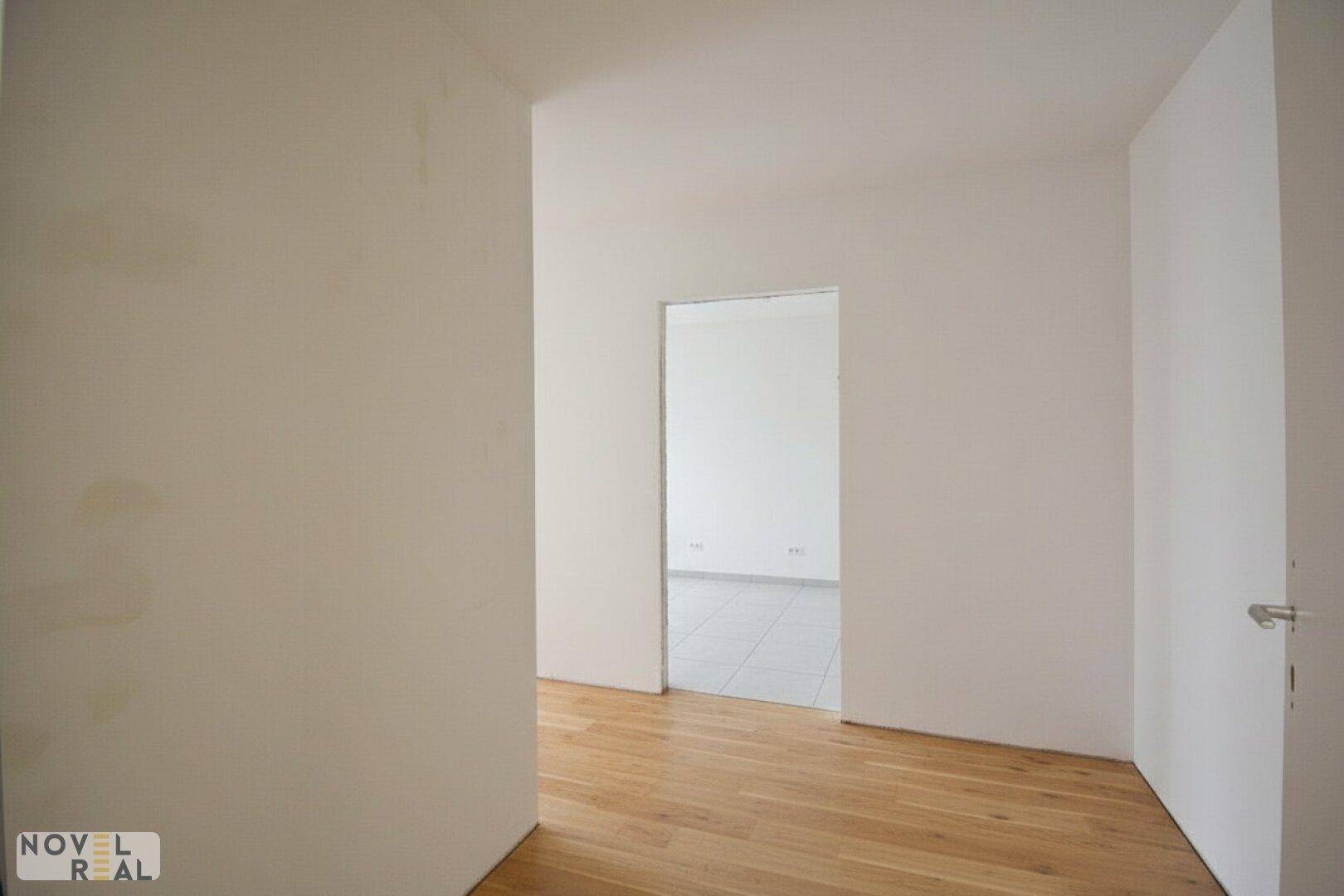 Heller Flur mit Holzfußboden, der zu einem weiteren Raum mit Fliesenboden führt.