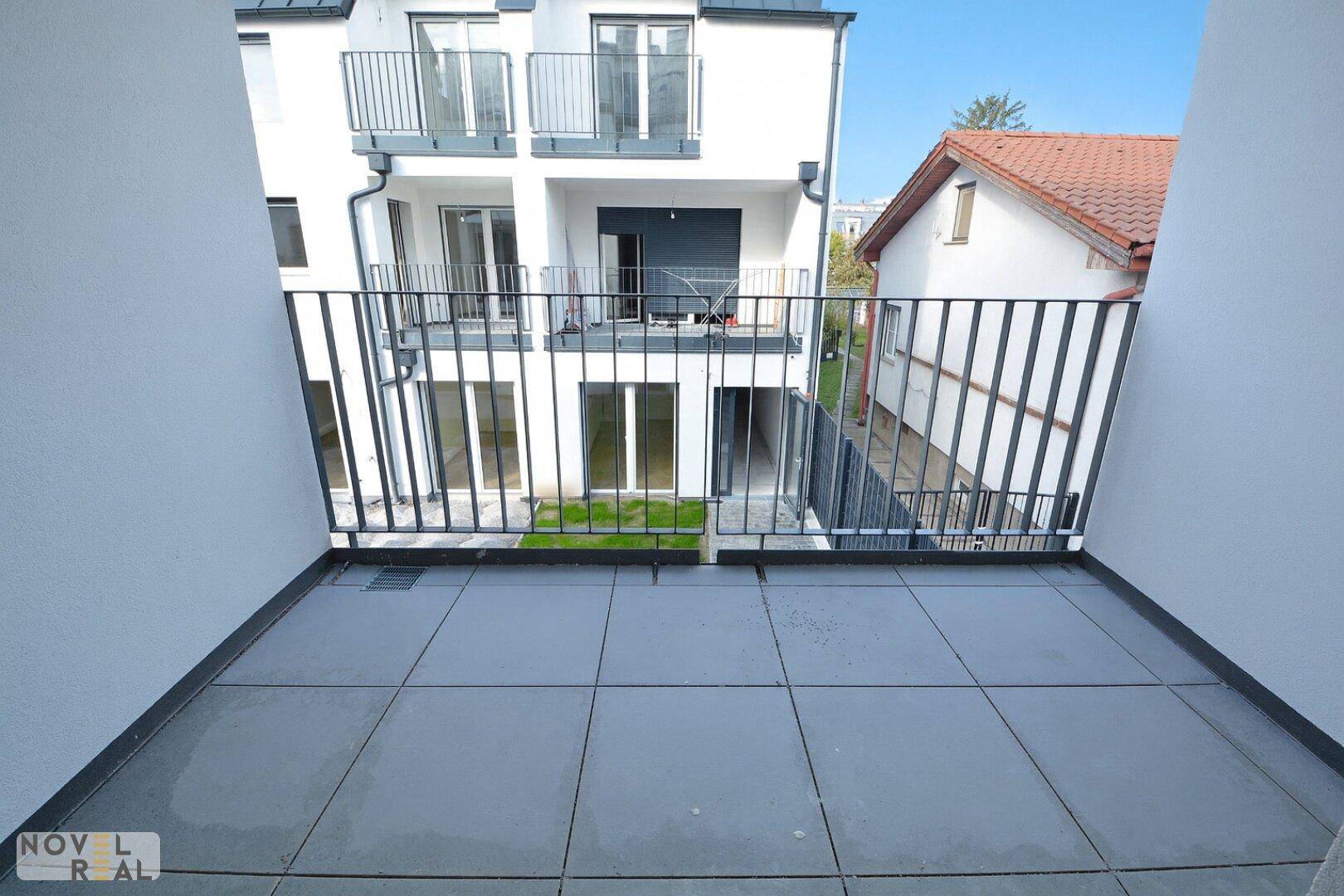 Balkon mit Fliesenboden und Blick auf den Innenhof und die umliegenden Gebäude.
