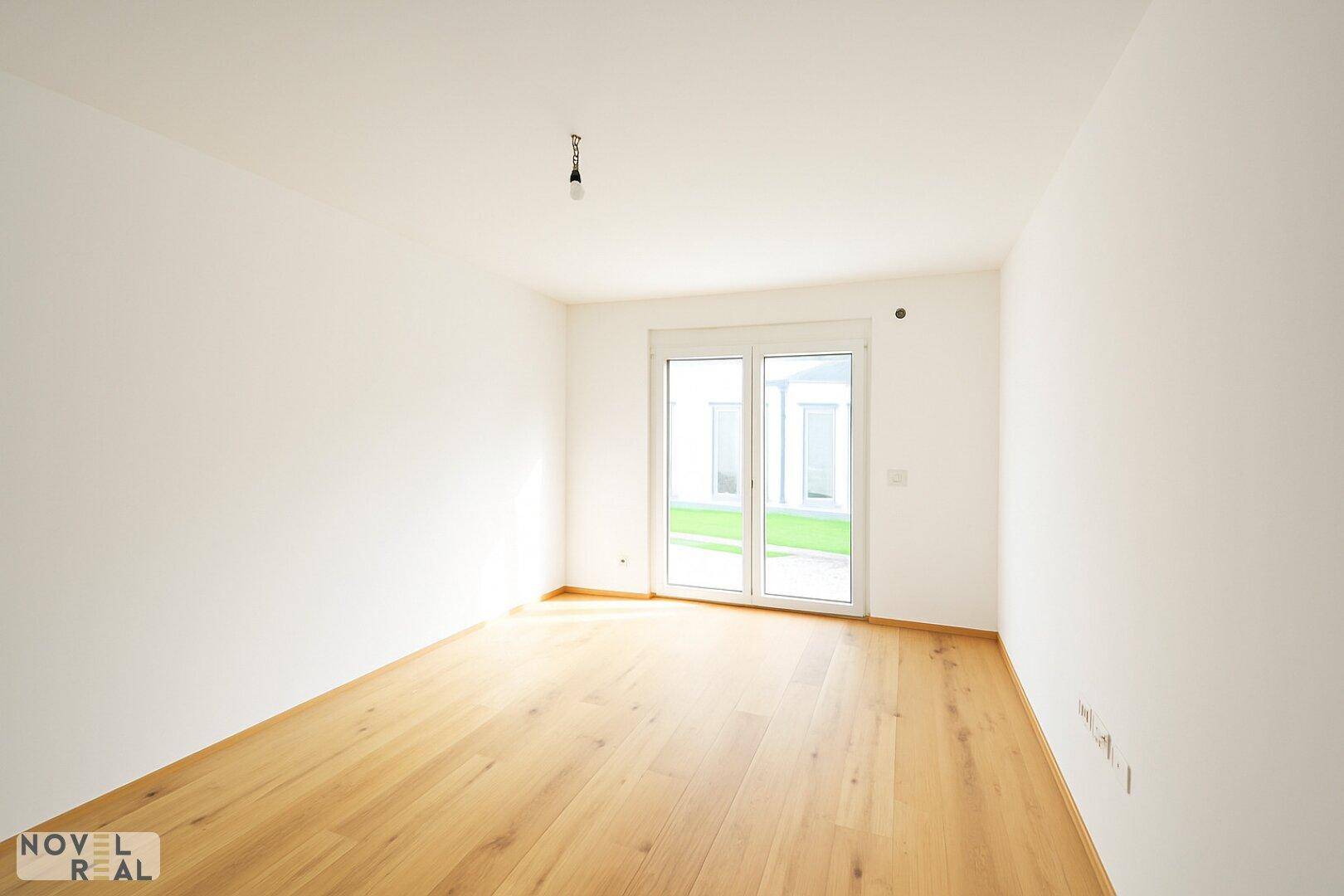 Leerer Raum mit Holzboden und großen Fenstern, die viel Tageslicht hereinlassen.