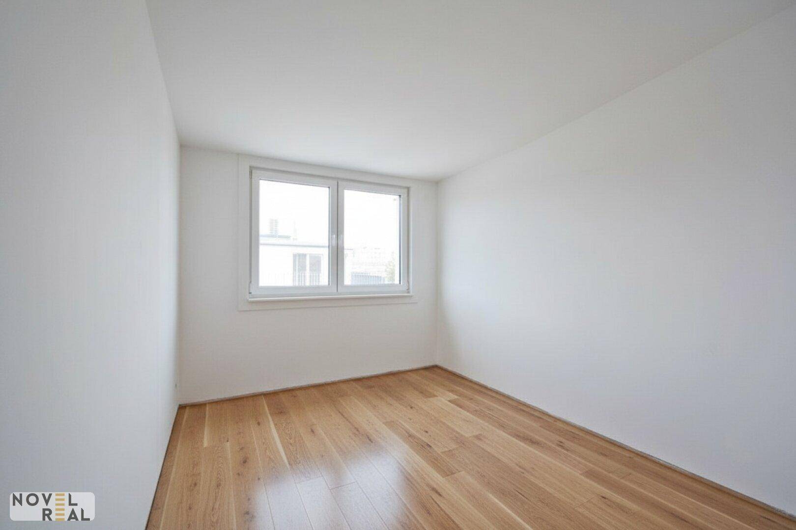 Helles, leeres Zimmer mit großen Fenstern und hochwertigem Holzboden, ideal als Schlafzimmer.