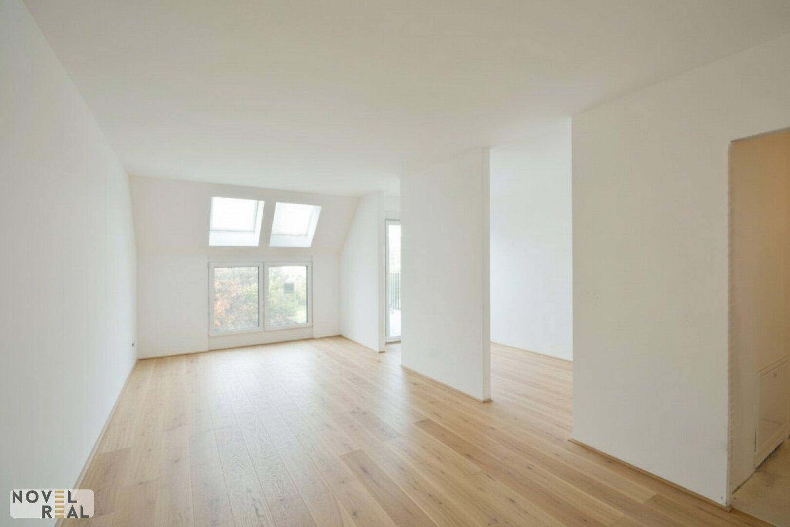 Leerer, lichtdurchfluteter Raum mit Dachschrägen, großen Fenstern und hellem Holzboden.