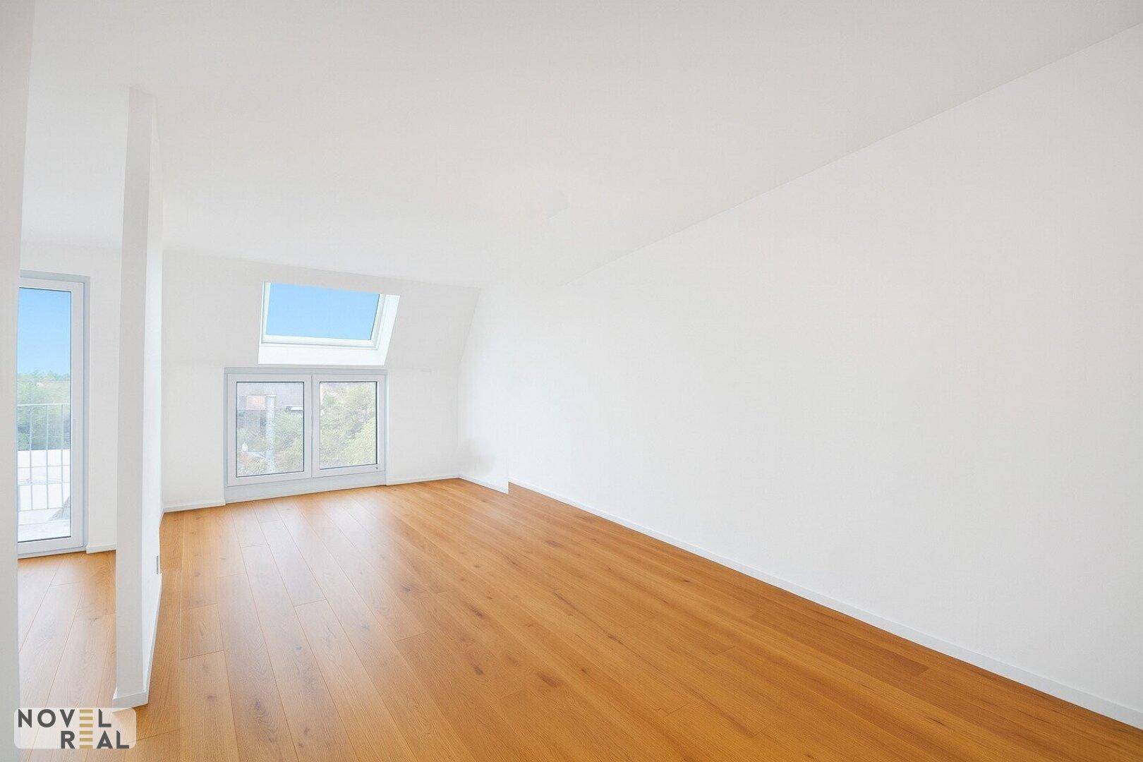 Helles, unmöbliertes Zimmer mit Holzboden, Dachschräge und großem Fenster, bietet viel Tageslicht.