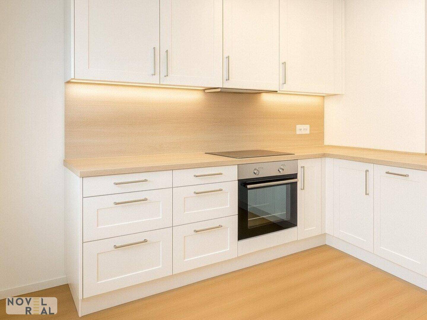 Moderne Einbauküche mit weißen Schränken, heller Holzoptik-Arbeitsplatte und integriertem Backofen.