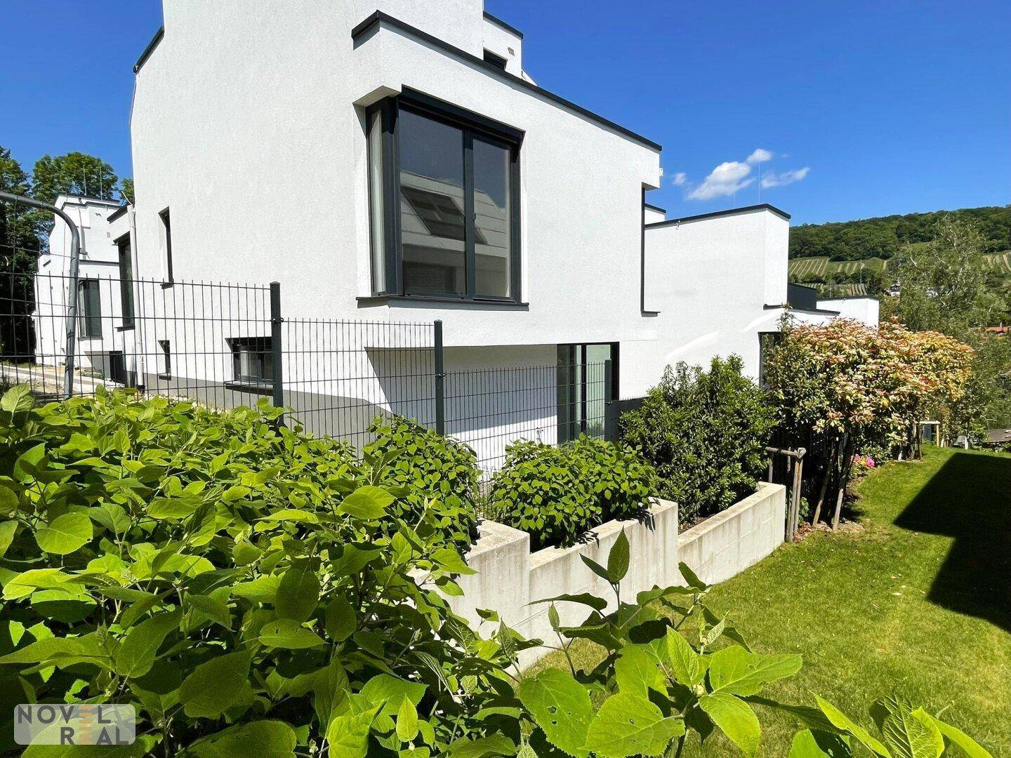Seitenansicht einer modernen Villa mit großen Fenstern und umgebender Bepflanzung.