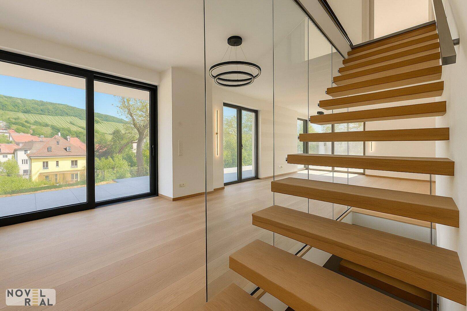 Lichtdurchfluteter Wohnbereich mit moderner Holztreppe und weitem Blick auf die Landschaft.