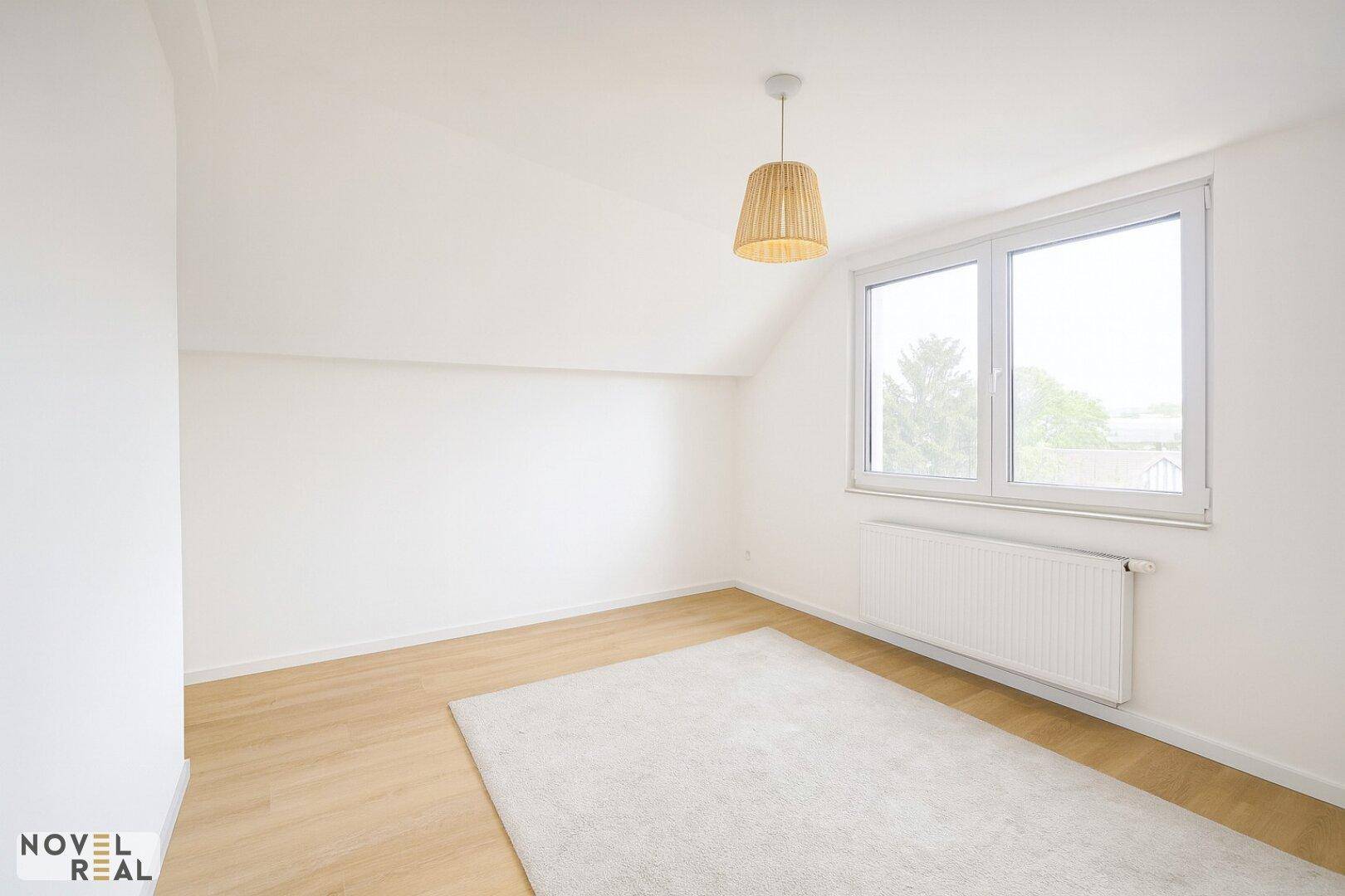 Helles Zimmer mit Dachschräge, Holzfußboden und großem Fenster, ideal als Schlafzimmer nutzbar.