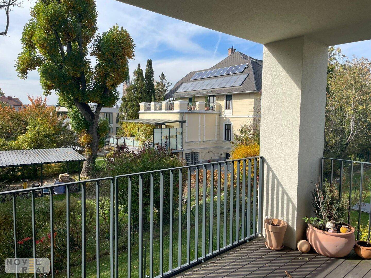 Blick vom Balkon auf eine grüne Umgebung mit Bäumen und einem Gebäude mit Solaranlage.