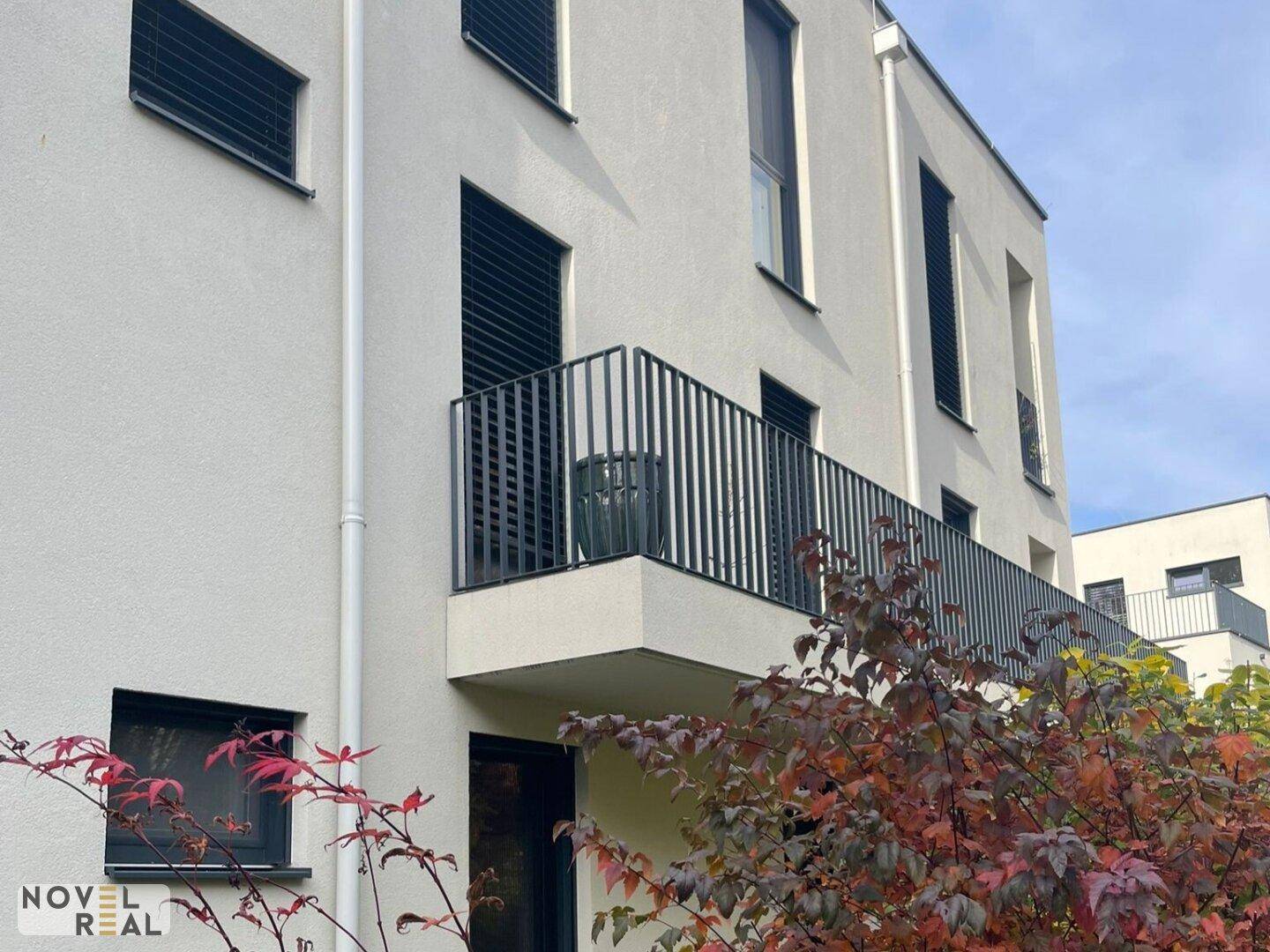 Moderne Gebäudefassade mit hellen Wänden, dunklen Fensterrahmen und Balkonen mit schwarzen Geländern.