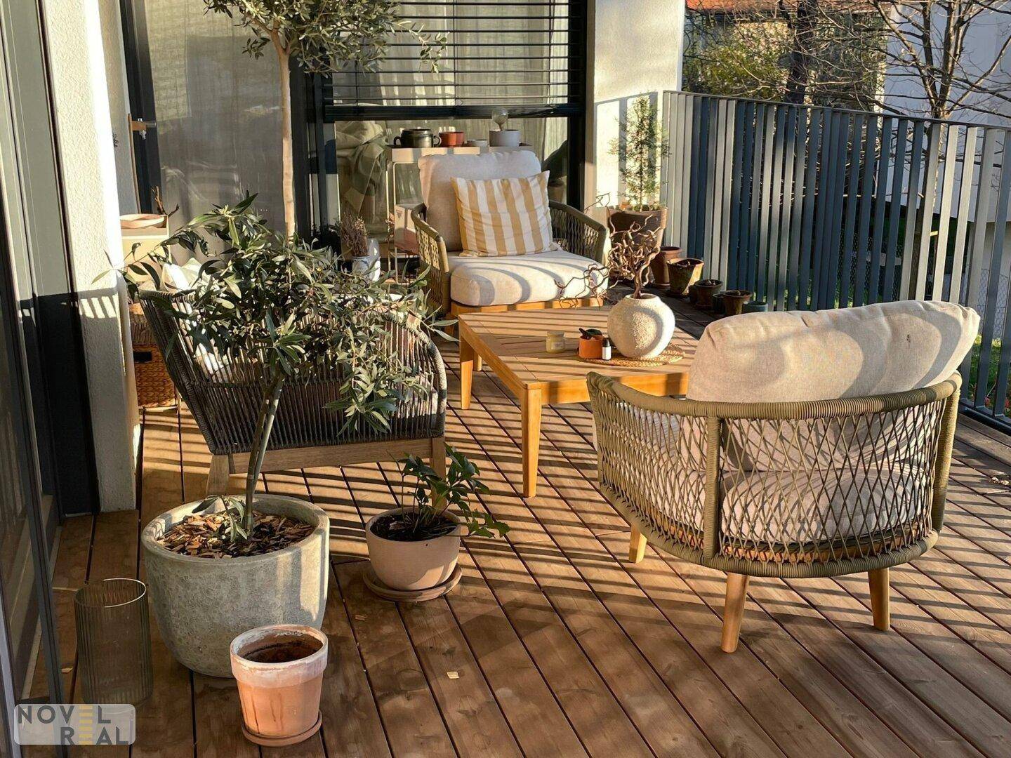 Sonniger Balkon mit Holzboden, gemütlichen Lounge-Möbeln und Topfpflanzen für entspannte Stunden.