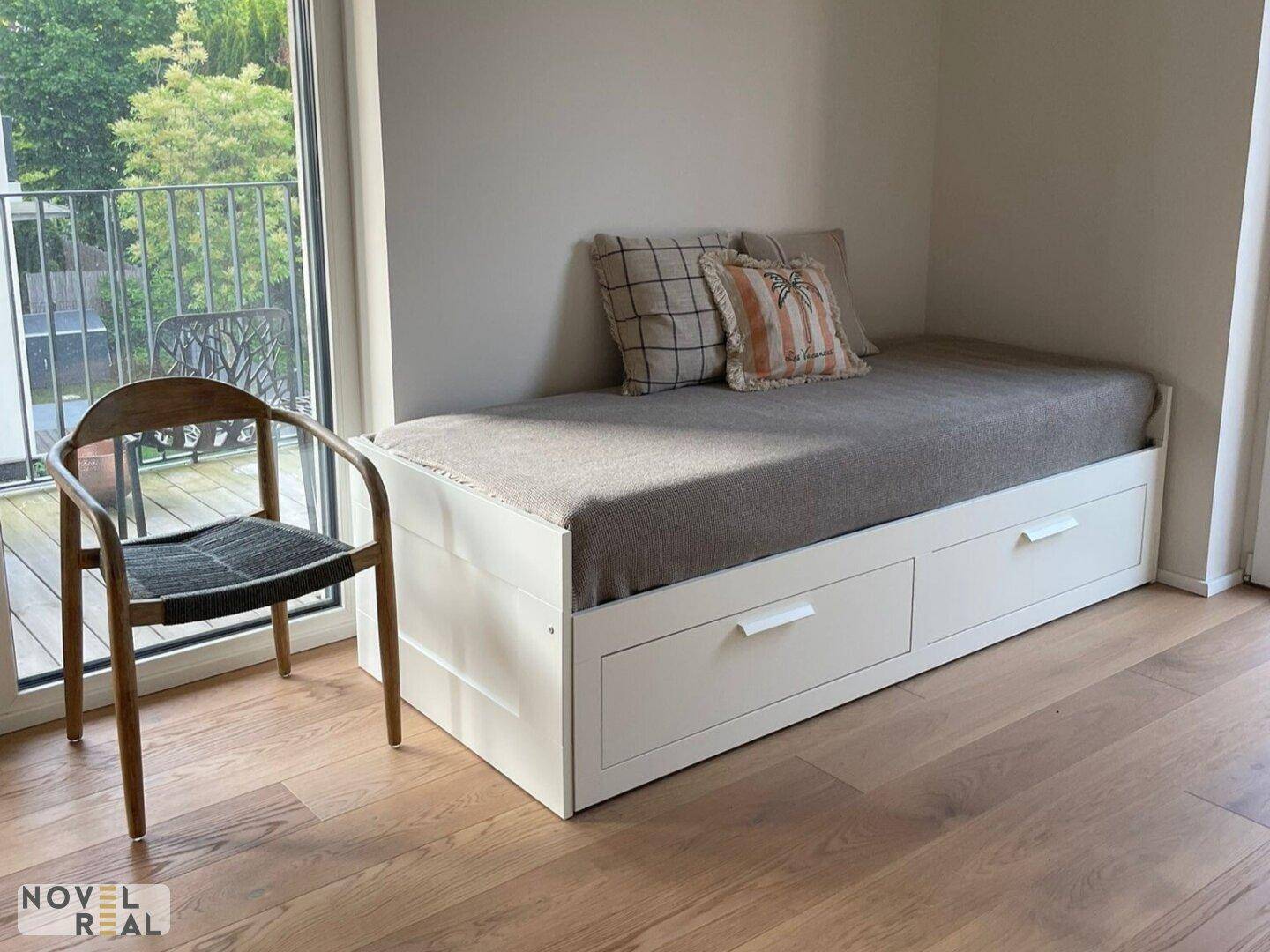 Helles Schlafzimmer mit Holzboden, Tagesbett mit Stauraum und Zugang zum Balkon.