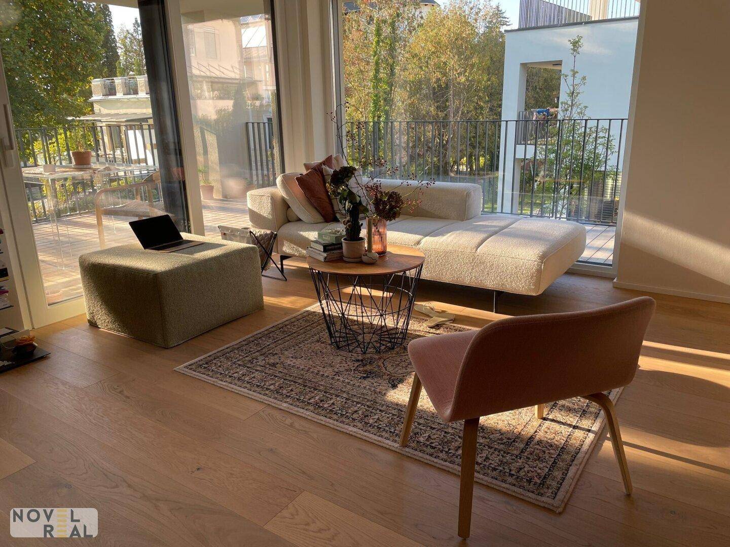 Lichtdurchflutetes Wohnzimmer mit hellem Parkettboden, modernem Sofa und Zugang zum Balkon.