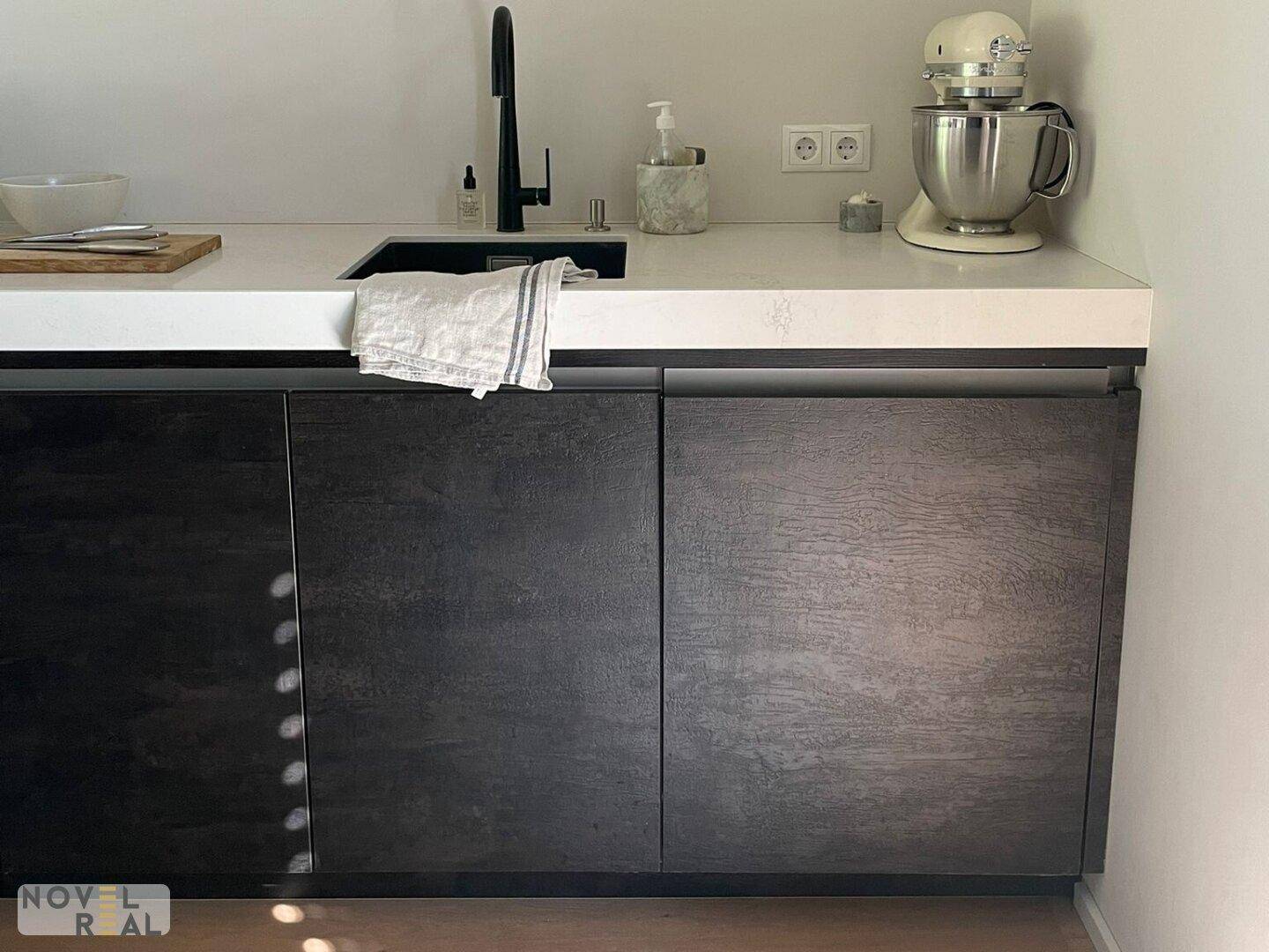 Moderne Küche mit dunklen Holzfronten, weißer Arbeitsplatte und integriertem Spülbecken.