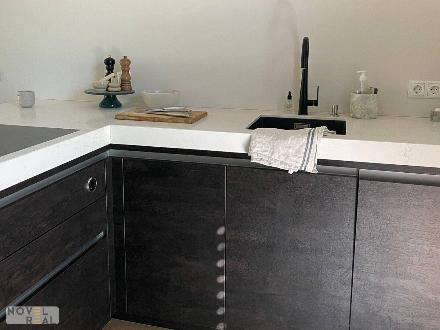 Stilvolle Küche mit dunklen Schränken, heller Arbeitsplatte und modernen Armaturen.