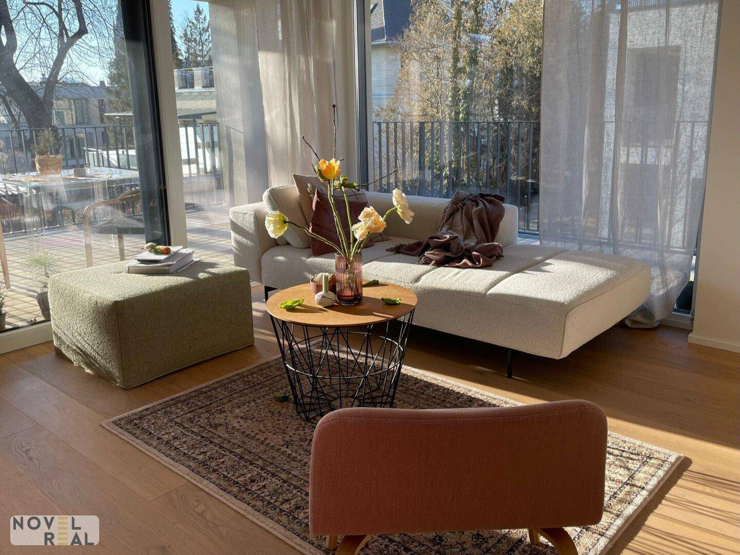 Sonniger Wohnbereich mit hellem Sofa, Teppich und Zugang zu einem großen Balkon.
