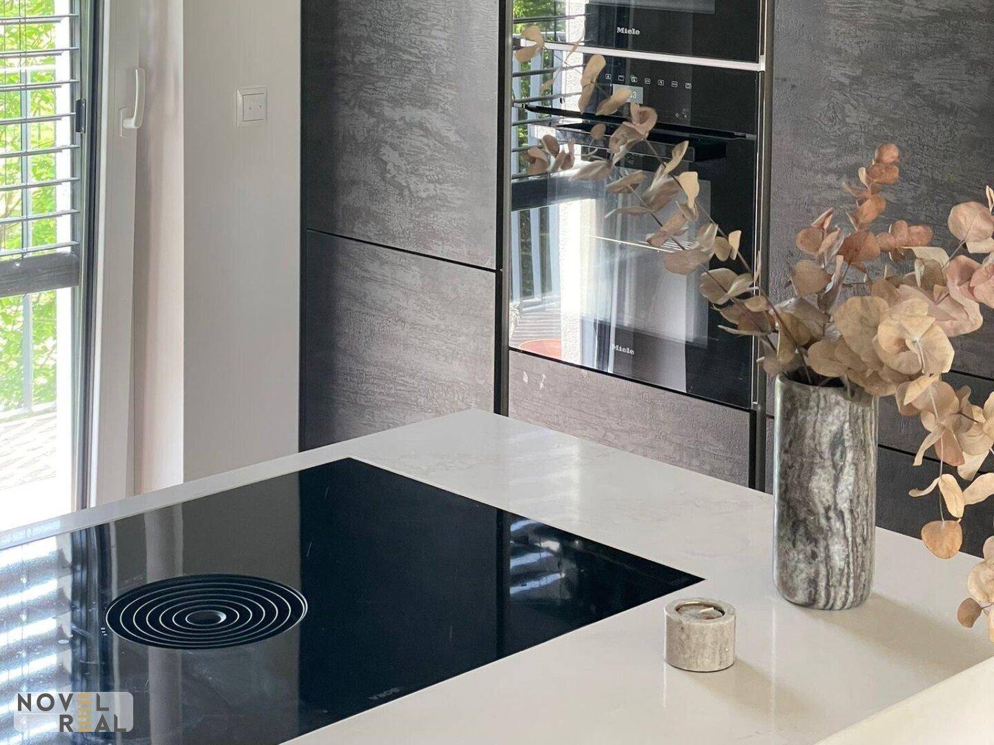 Hochwertige Küche mit Induktionskochfeld, integrierten Miele-Geräten und weißer Arbeitsplatte.