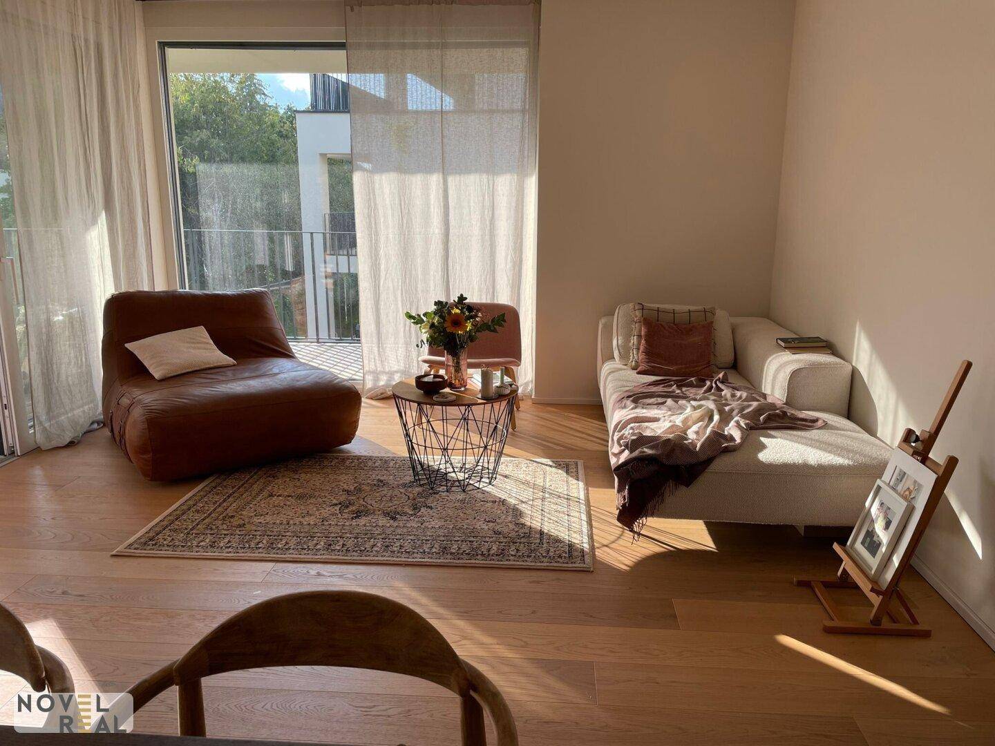 Sonniger Wohnbereich mit beigem Sofa, braunem Ledersessel und Zugang zum Außenbereich.