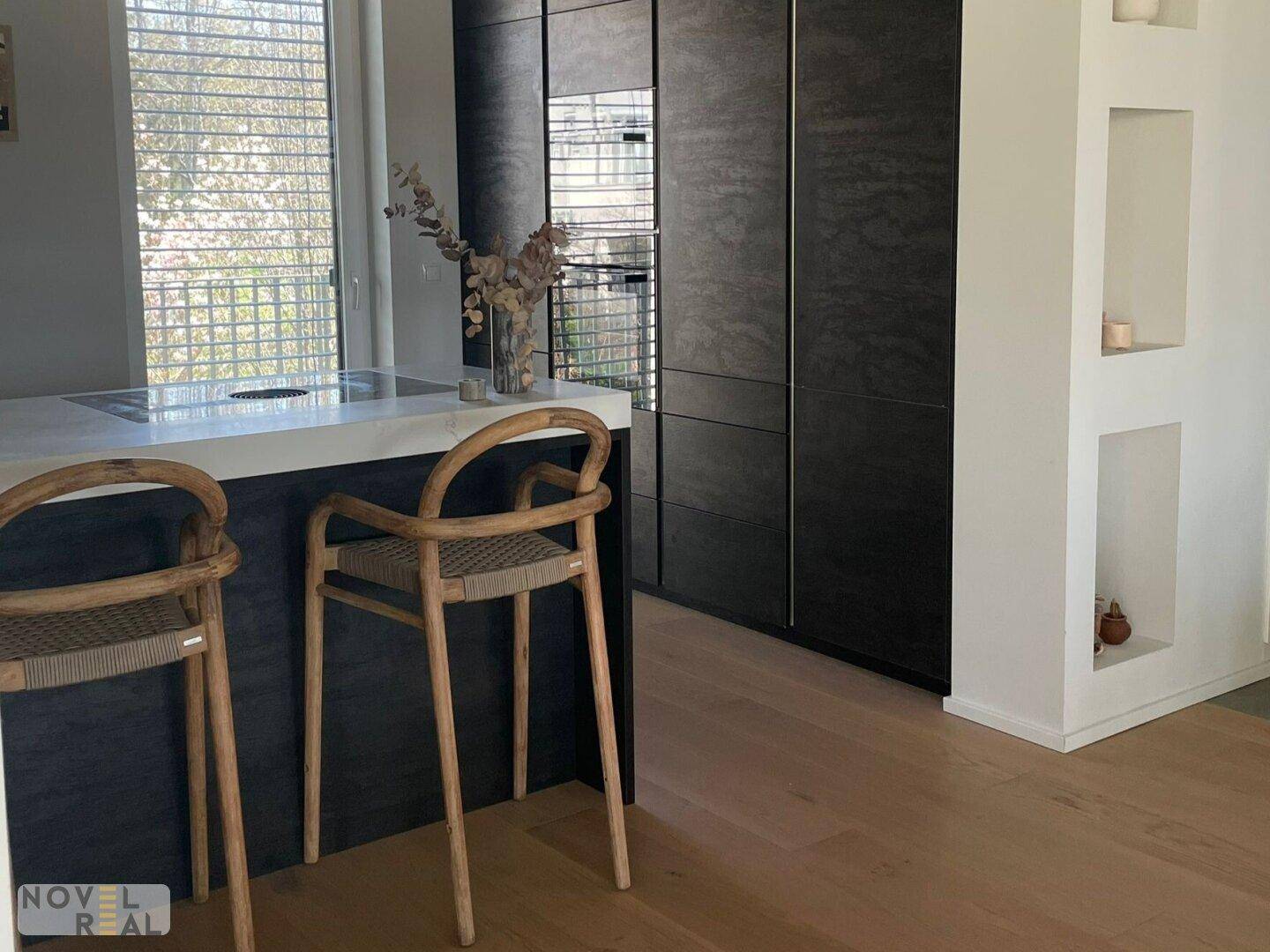 Offene Küche mit Bartheke, modernen Hockern und integrierten Geräten, verbunden mit dem Wohnbereich.