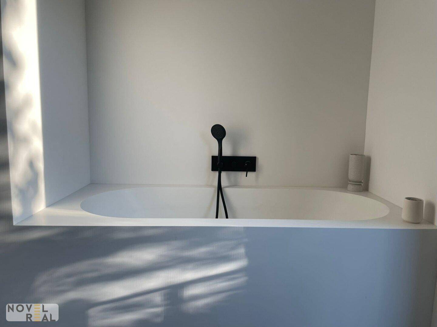 Modernes Badezimmer mit integrierter Badewanne und schwarzen Armaturen in minimalistischem Design.