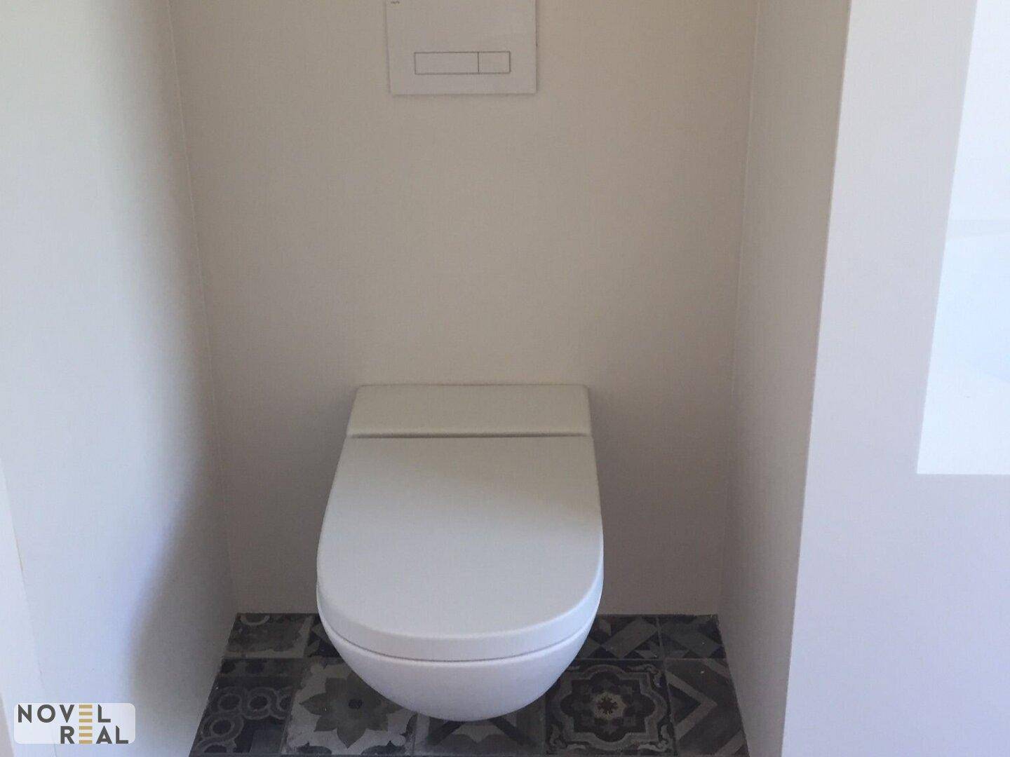 Separate Toilette mit Wand-WC und gemusterten Bodenfliesen in modernem Stil.