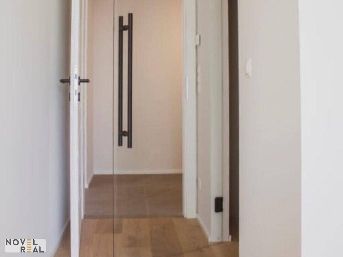 Heller Flur mit Holzboden und moderner Glastür, die zu weiteren Räumen führt.