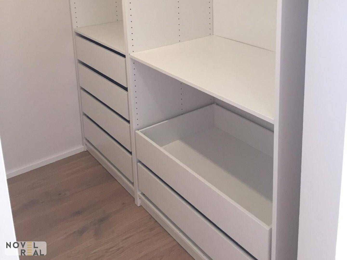 Begehbarer Kleiderschrank mit weißen Regalen und Schubladen für organisierte Aufbewahrung.