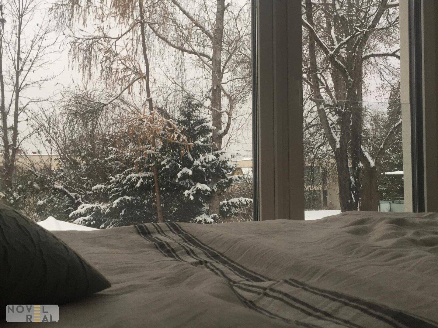 Gemütliches Schlafzimmer mit Blick auf eine verschneite Winterlandschaft durch große Fenster.