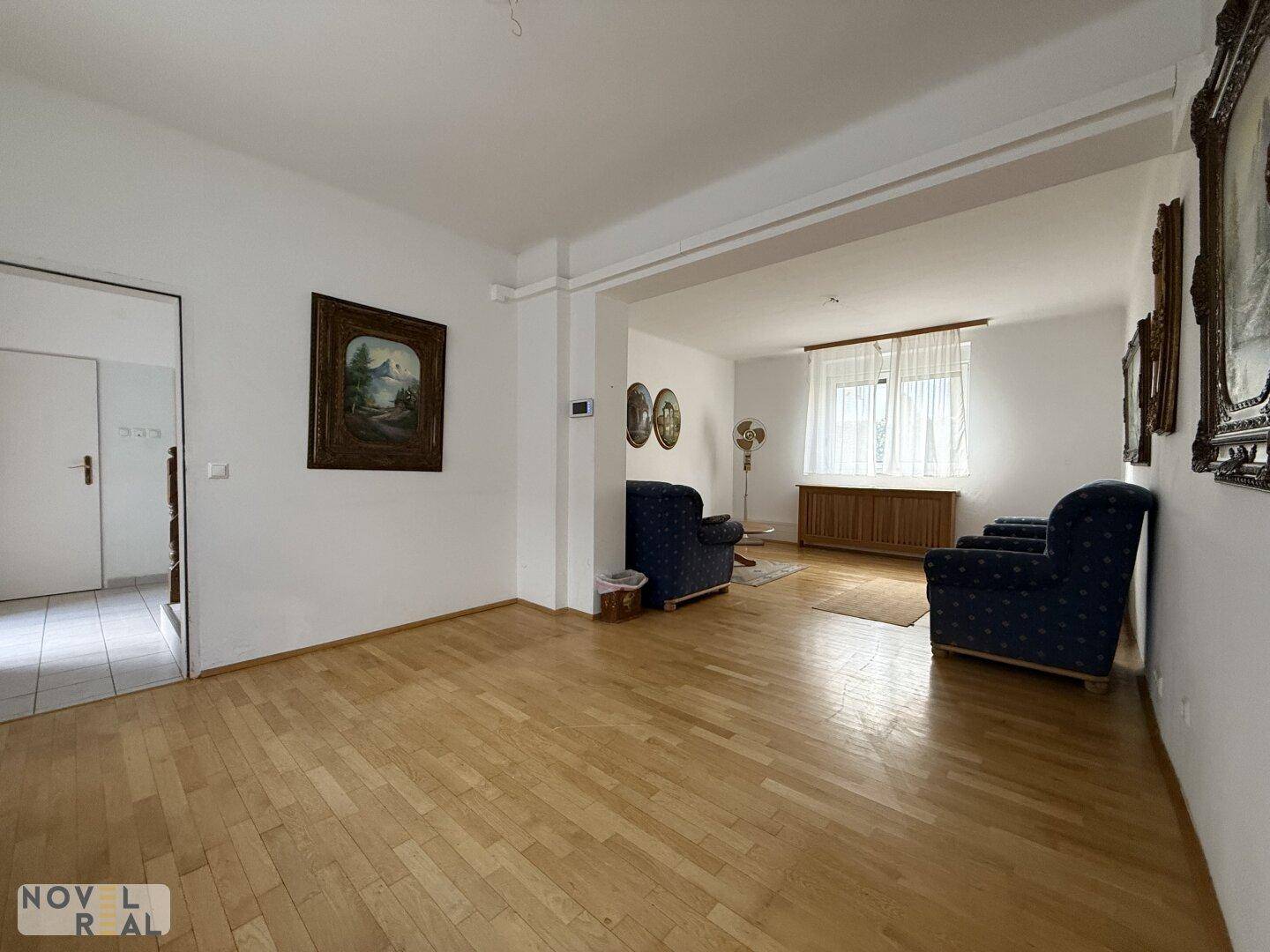 Geräumiges Wohnzimmer mit Parkettboden und traditionellen Gemälden an den weißen Wänden.