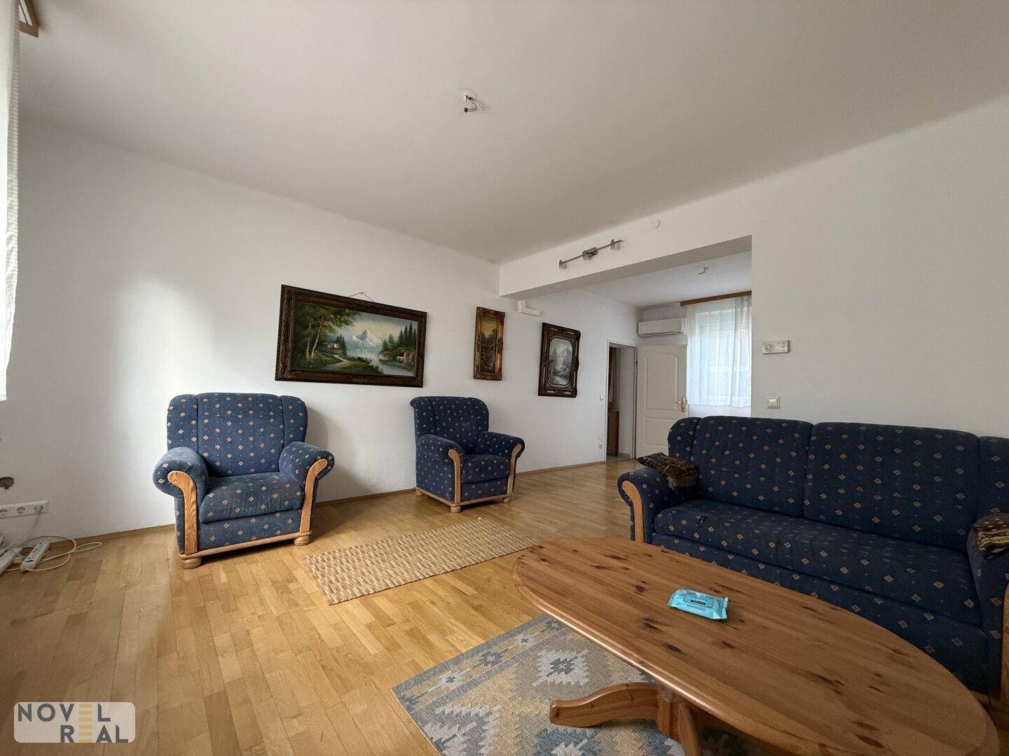 Gemütliches Wohnzimmer mit blauen Polstermöbeln, Holzboden und einem ovalen Couchtisch.